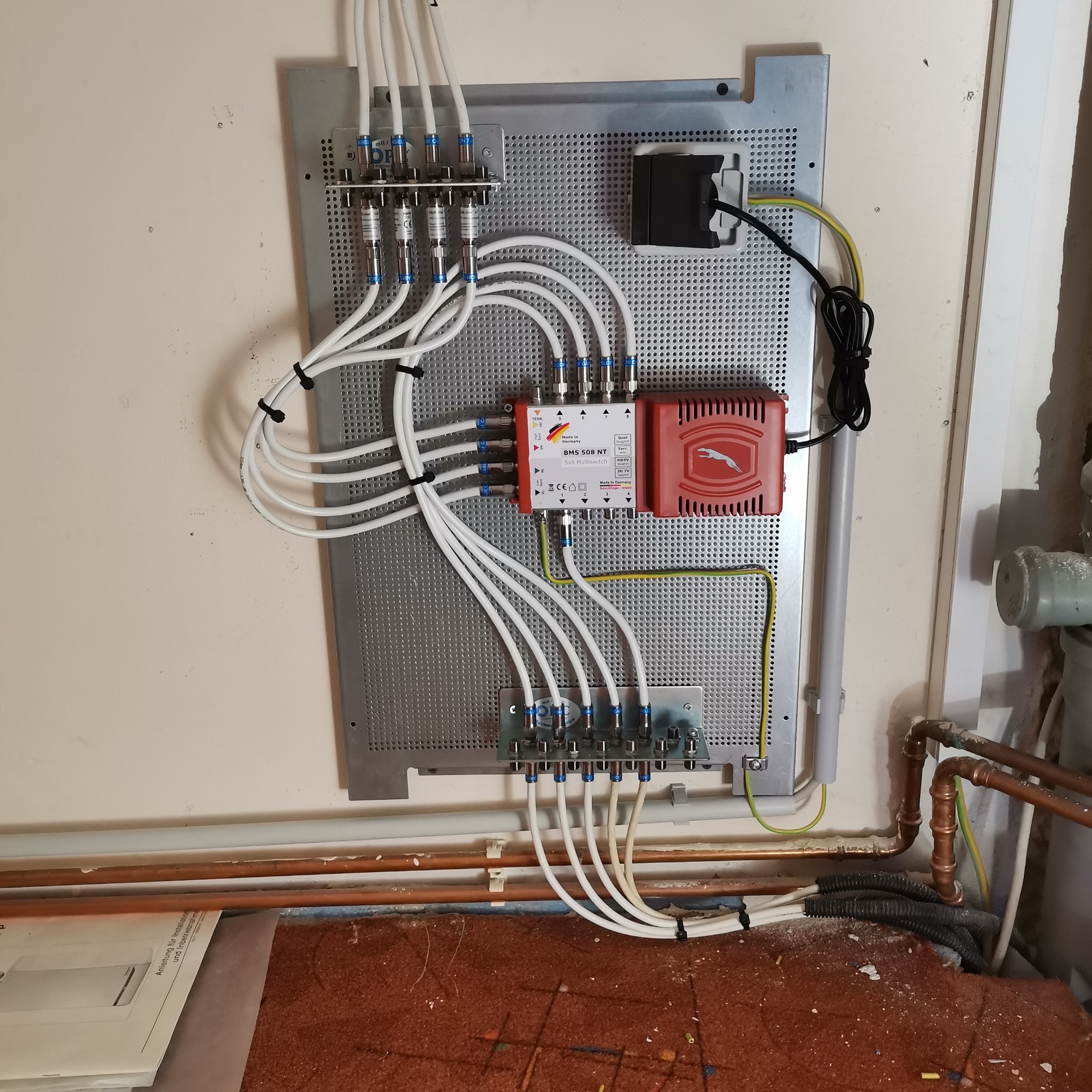 Szczegółowe ujęcie instalacji multiswitcha BMS 508 NT na perforowanej płycie montażowej, z podłączonymi białymi kablami koncentrycznymi z niebieskimi złączkami, widoczne także przewody uziemiające...