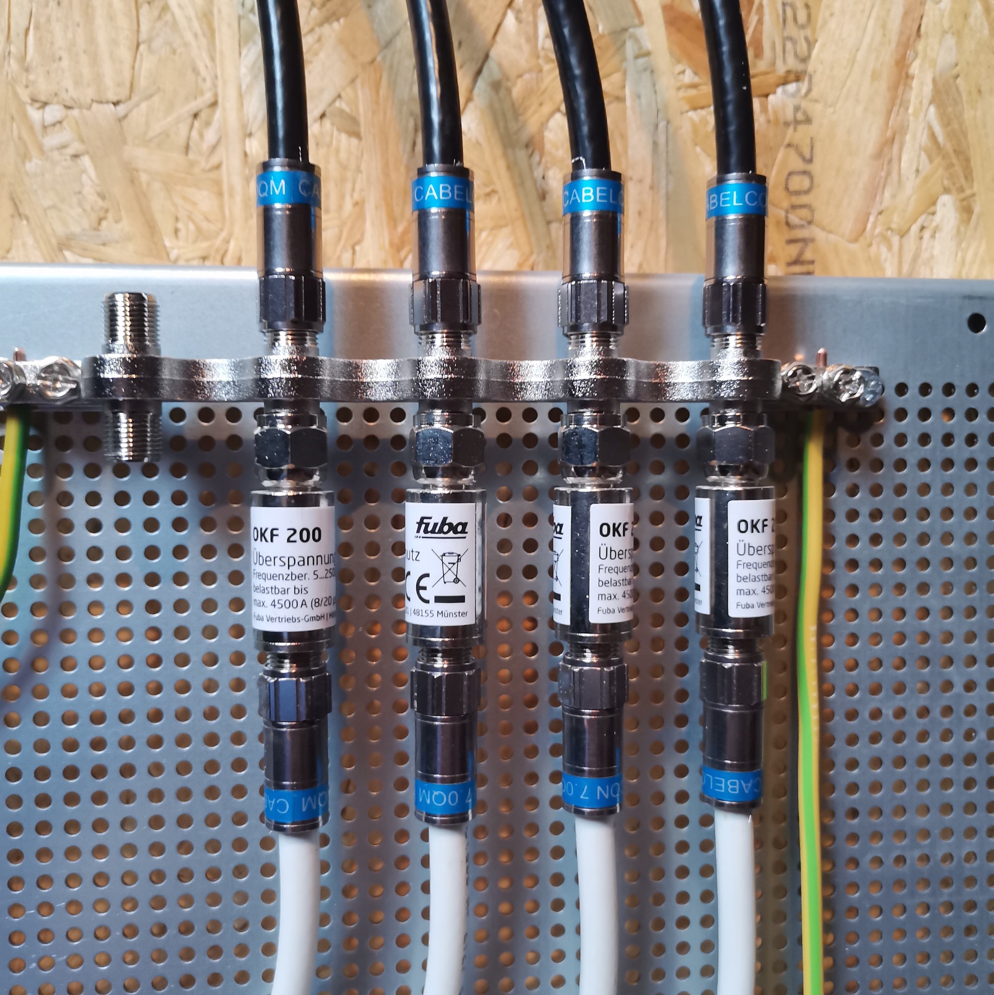 Cztery kable antenowe podłączone do listwy z zabezpieczeniami przepięciowymi Fuba OKF 200, zamocowane na perforowanej płycie z uziemieniem.