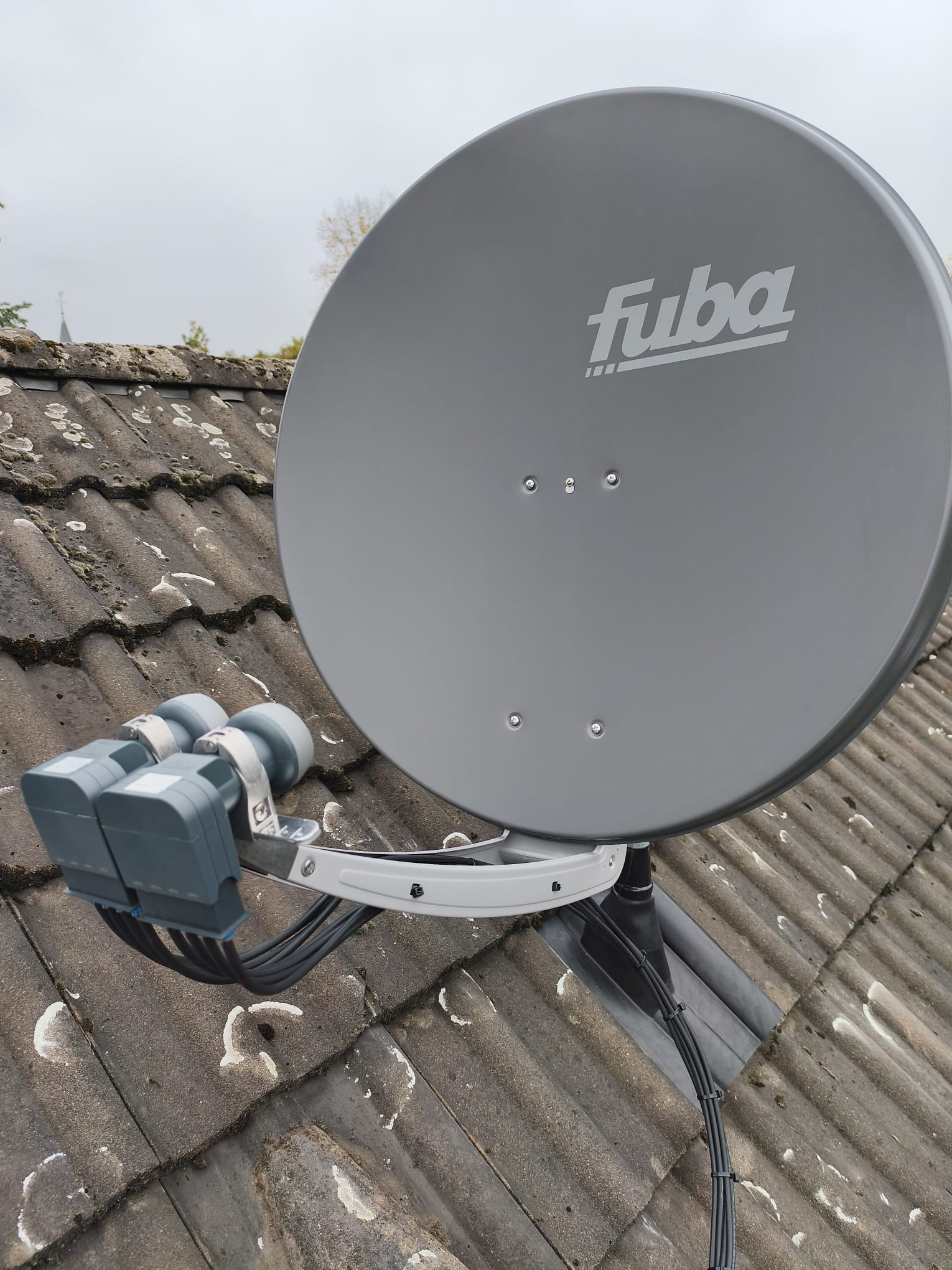 Antena satelitarna Fuba z podwójnym konwerterem na dachu pokrytym dachówką, Dortmund. Widok z dołu, pochmurne niebo w tle.