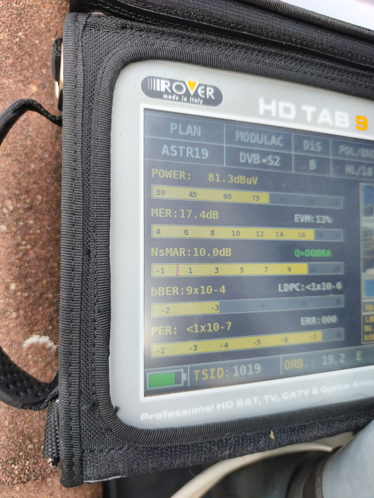 Miernik sygnału satelitarnego Rover HD TAB 9 w czarnym futerale, wyświetlający parametry sygnału ASTR19, DVB-S2, z widocznymi wartościami mocy, MER i NsMAR.