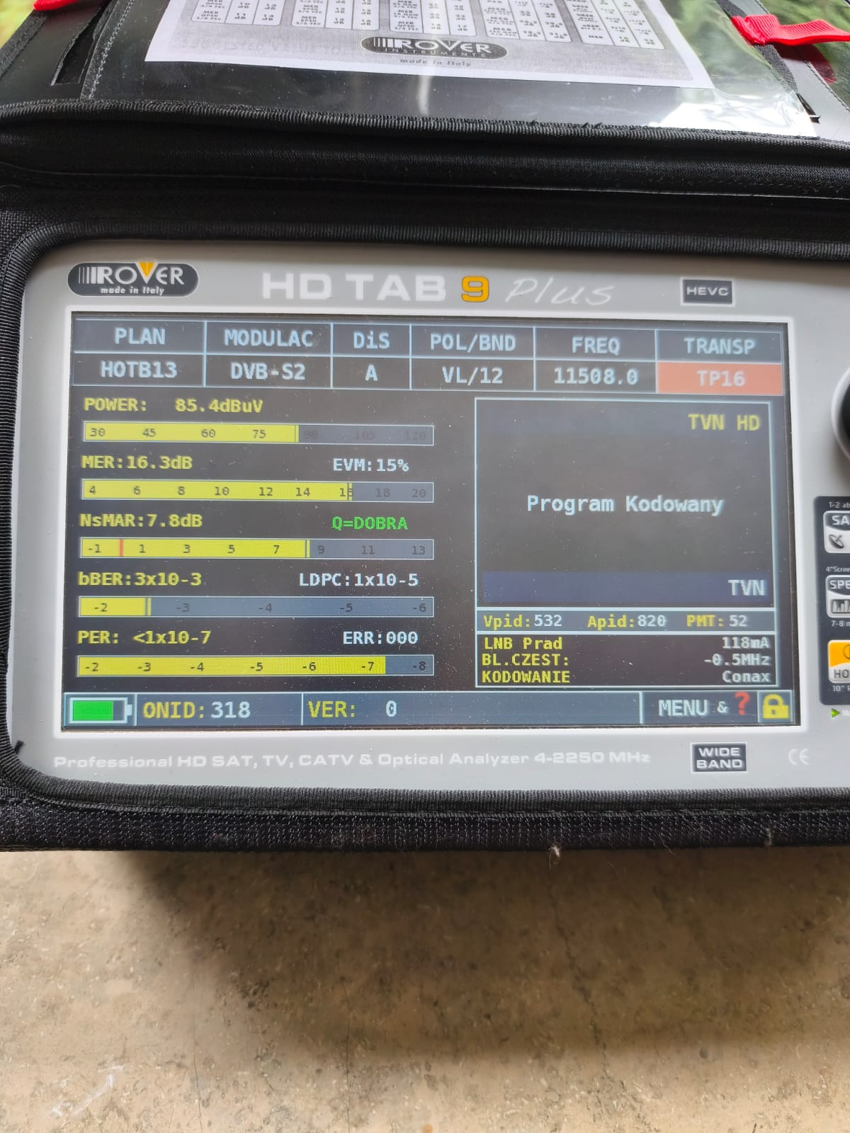 Analizator sygnału satelitarnego Rover HD TAB 9 Plus w czarnym futerale, wyświetlający parametry sygnału TVN HD. Widoczne wartości mocy, MER, EVM i inne.