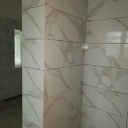 Układanie płytek imitujących marmur na ścianach łazienki, widoczne krzyżyki dystansowe, wnętrze w trakcie remontu.