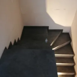 Schody wyłożone ciemną płytką, widok z g&oacute;ry, z butelką wody na jednym ze stopni. Część stopni wykończona białym pasem.