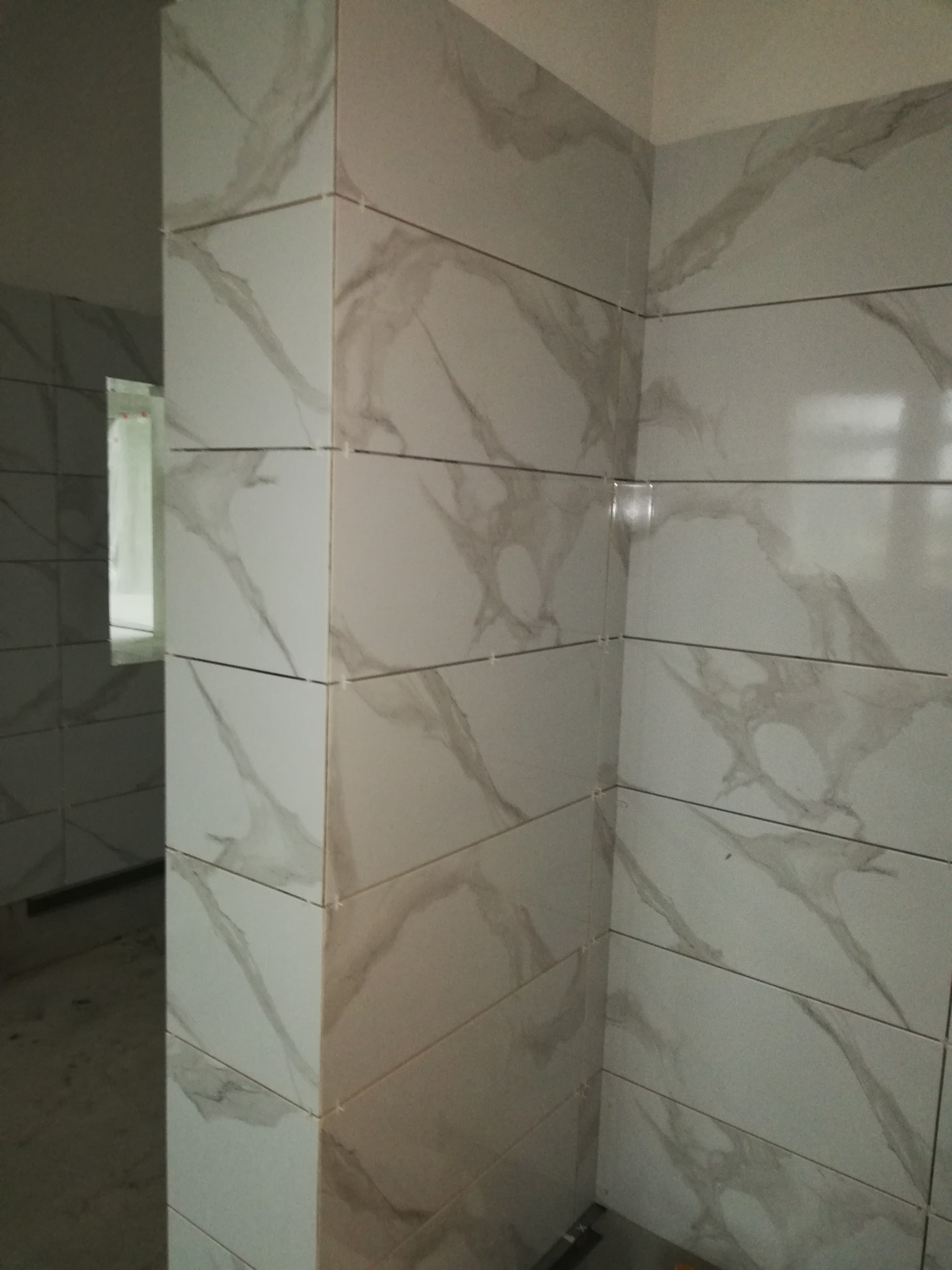 Układanie płytek imitujących marmur na ścianach łazienki, widoczne krzyżyki dystansowe, wnętrze w trakcie remontu.