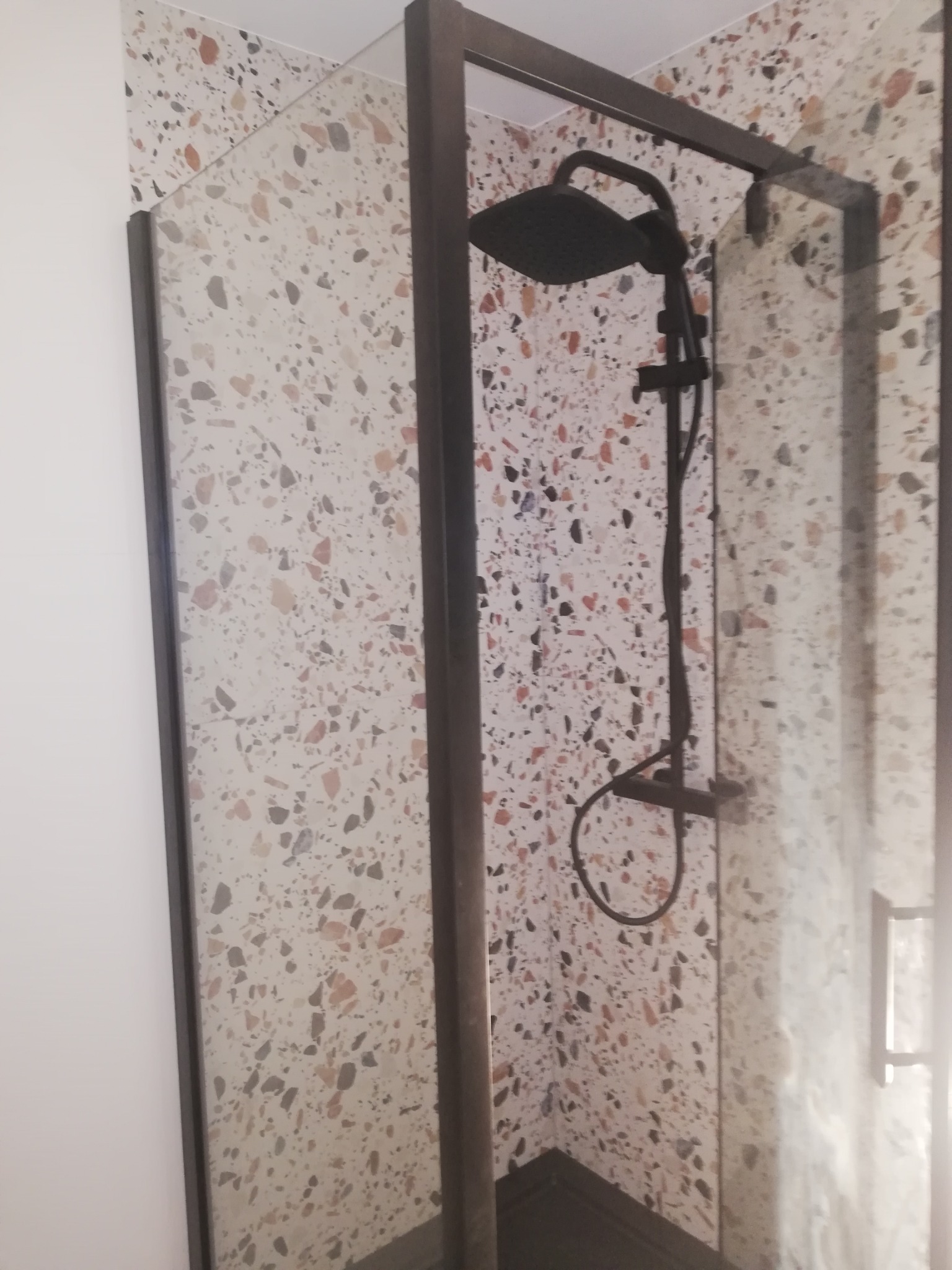 Kabina prysznicowa z czarną armaturą na tle ściany wykończonej płytkami imitującymi lastryko.