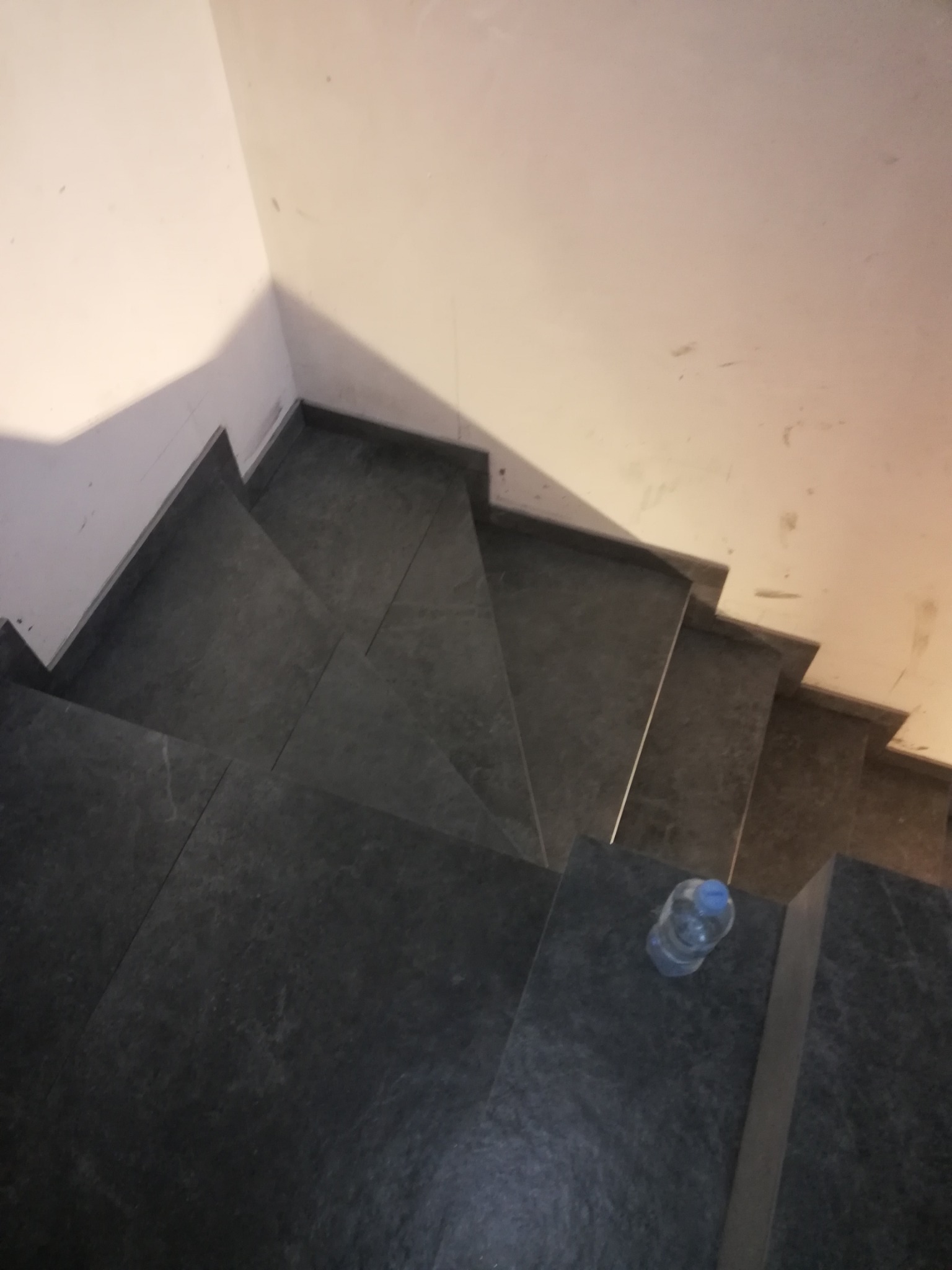 Schody wyłożone ciemnoszarą płytką, widok z góry, na jednym ze stopni leży butelka wody.