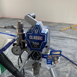 WKBUD - Profesjonalny agregat malarski Graco Classic 390 PC, z manometrem wskazującym ciśnienie, ustawiony na folii ochronnej w trakcie malowania wnętrza.