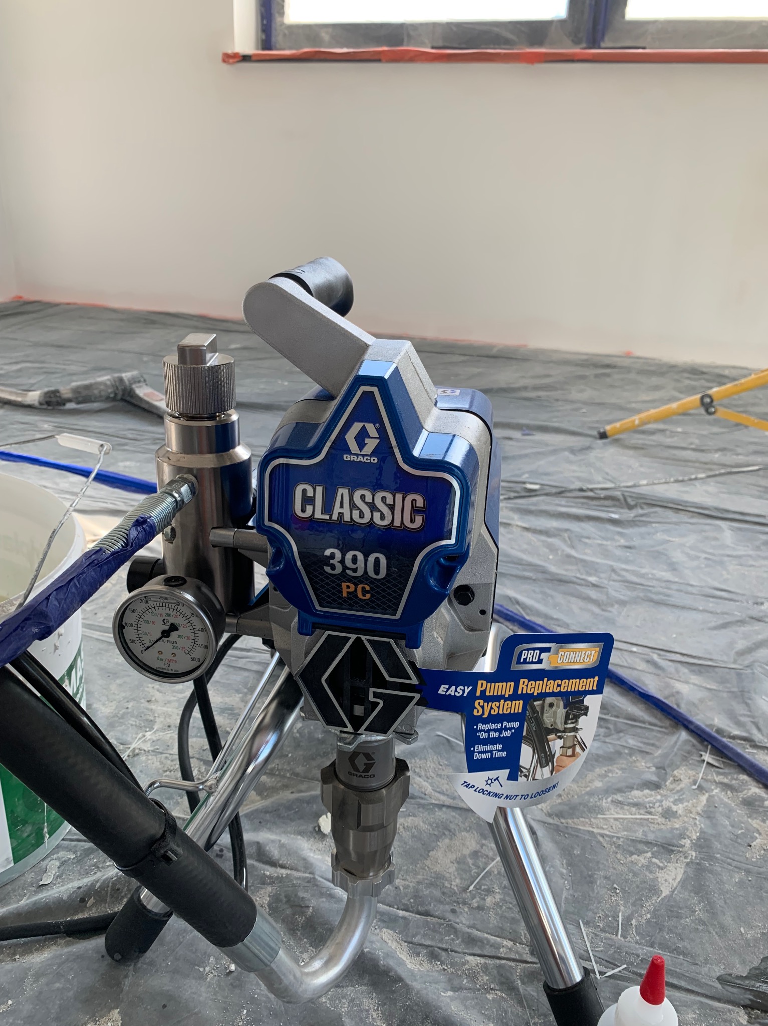 Profesjonalny agregat malarski Graco Classic 390 PC, z manometrem wskazującym ciśnienie, ustawiony na folii ochronnej w trakcie malowania wnętrza.