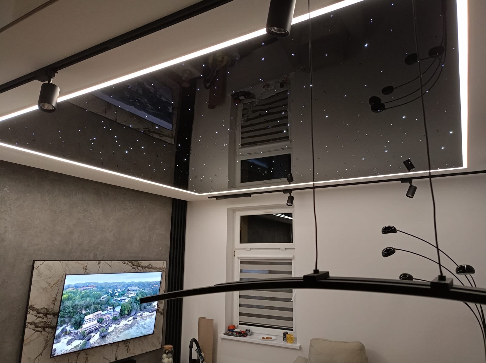 Salon z czarnym, lustrzanym sufitem podwieszanym z efektem gwiazd, oświetlonym listwami LED, szynoprzewodem z reflektorami i nowoczesną lampą wiszącą.