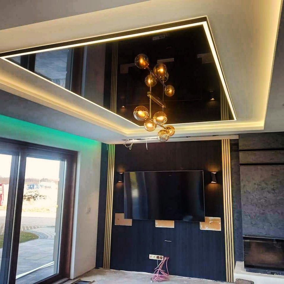 Nowoczesny salon w trakcie wykańczania: podwieszany sufit z lustrzanym panelem i oświetleniem LED, designerska lampa wisząca z kulistymi kloszami, ściana z ciemnego drewna z elementami...