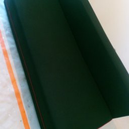 NT Detailing Profesjonalne Czyszczenie Tapicerki - Ciemnozielona kanapa z czerwoną lamówką stoi na zabezpieczonej folią podłodze, gotowa do użytku po czyszczeniu.