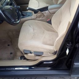 NT Detailing Profesjonalne Czyszczenie Tapicerki - Wnętrze samochodu Volvo z beżową tapicerką przednich foteli i dywaników, widoczne zabrudzenia na siedzeniu kierowcy, otwarte drzwi.