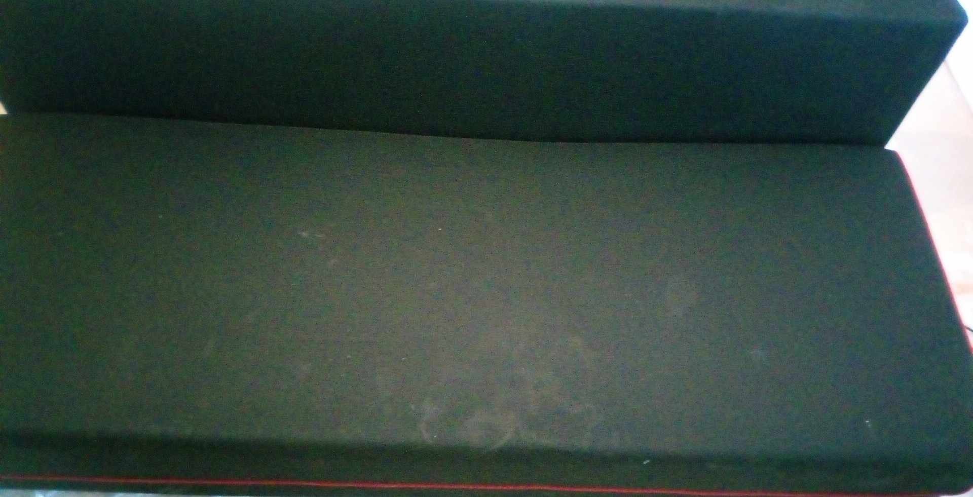 Ciemnozielona tapicerka kanapy z widocznymi plamami i czerwoną lamówką u dołu