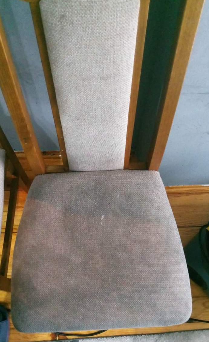 Krzesło z drewnianą ramą i tapicerowanym siedziskiem, widoczne plamy na siedzisku przed czyszczeniem, szara tapicerka z wyraźnym wzorem tkaniny.