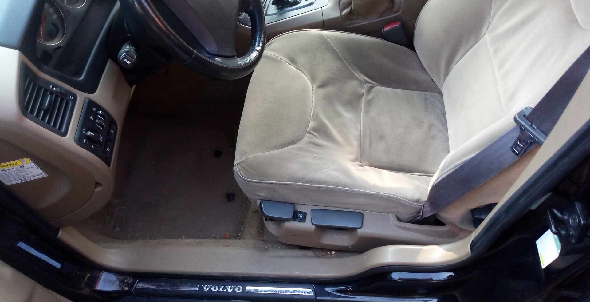 Brudne, beżowe siedzenie kierowcy w samochodzie marki Volvo, widoczne ślady użytkowania i zabrudzenia na tapicerce oraz podłodze.