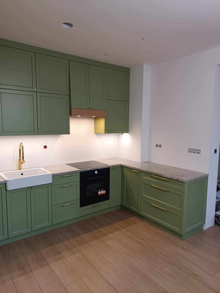 Kuchenna zabudowa w odcieniach zieleni z blatem imitującym marmur. Złota armatura i uchwyty dodają elegancji. Parkiet z naturalnego drewna.