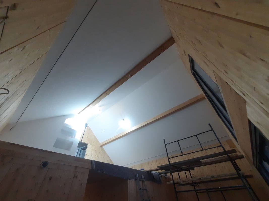 Poddasze z drewnianą konstrukcją i ocieplonym skośnym sufitem, widoczne rusztowanie i okno dachowe w trakcie prac wykończeniowych.