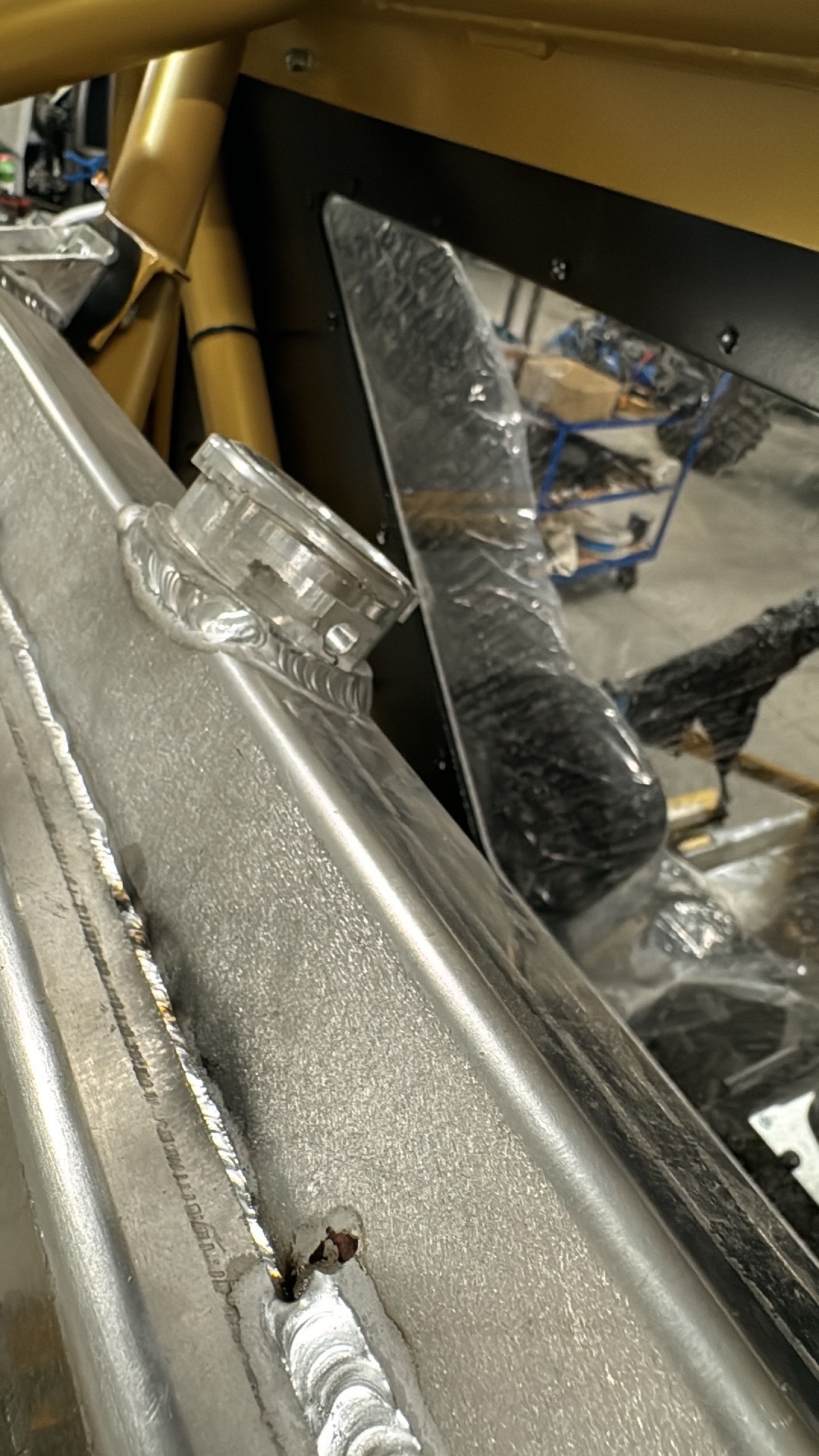 Fragment ramy pojazdu z widocznymi spawami i mocowaniem elementu, wykonany z metalu o srebrzystej barwie, z widocznymi niedoskonałościami spoin.