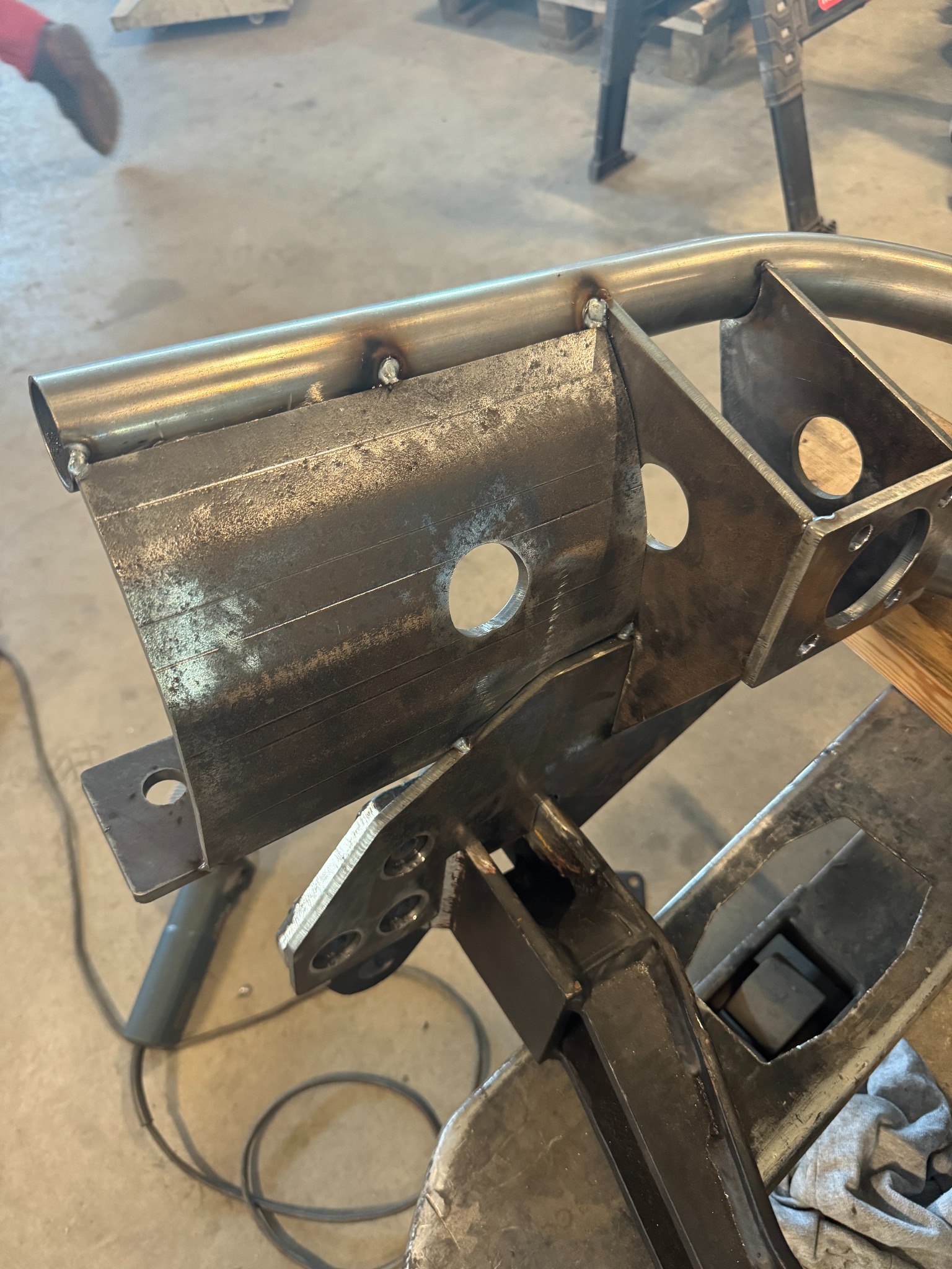 Fragment konstrukcji metalowej z widocznymi spawami i otworami, wykonanej w warsztacie w Więckowicach. Element w trakcie obróbki, leżący na stole roboczym.