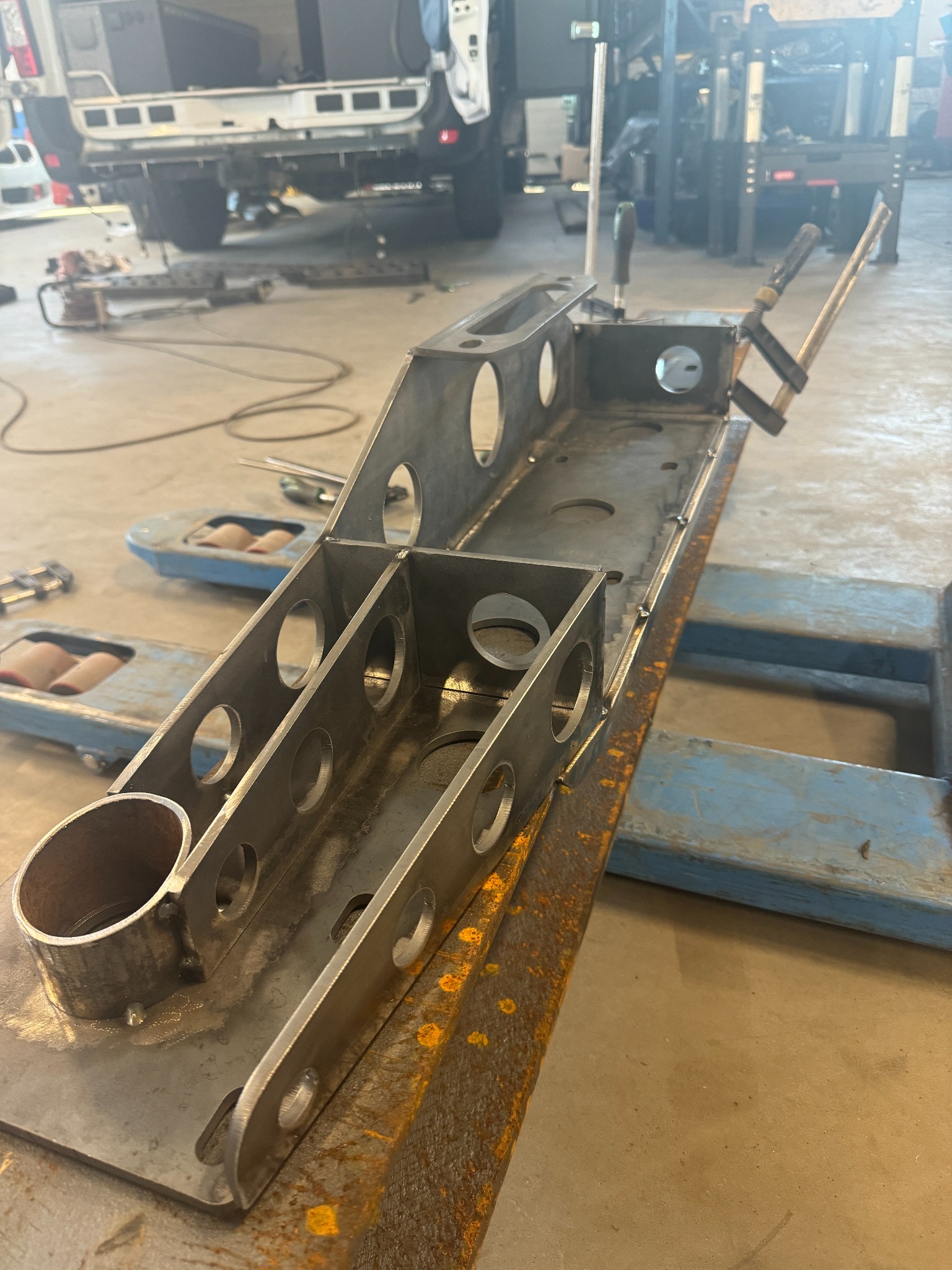 Metalowa konstrukcja z otworami, w trakcie procesu łączenia elementów, widoczne ślady spawania i narzędzia w tle.