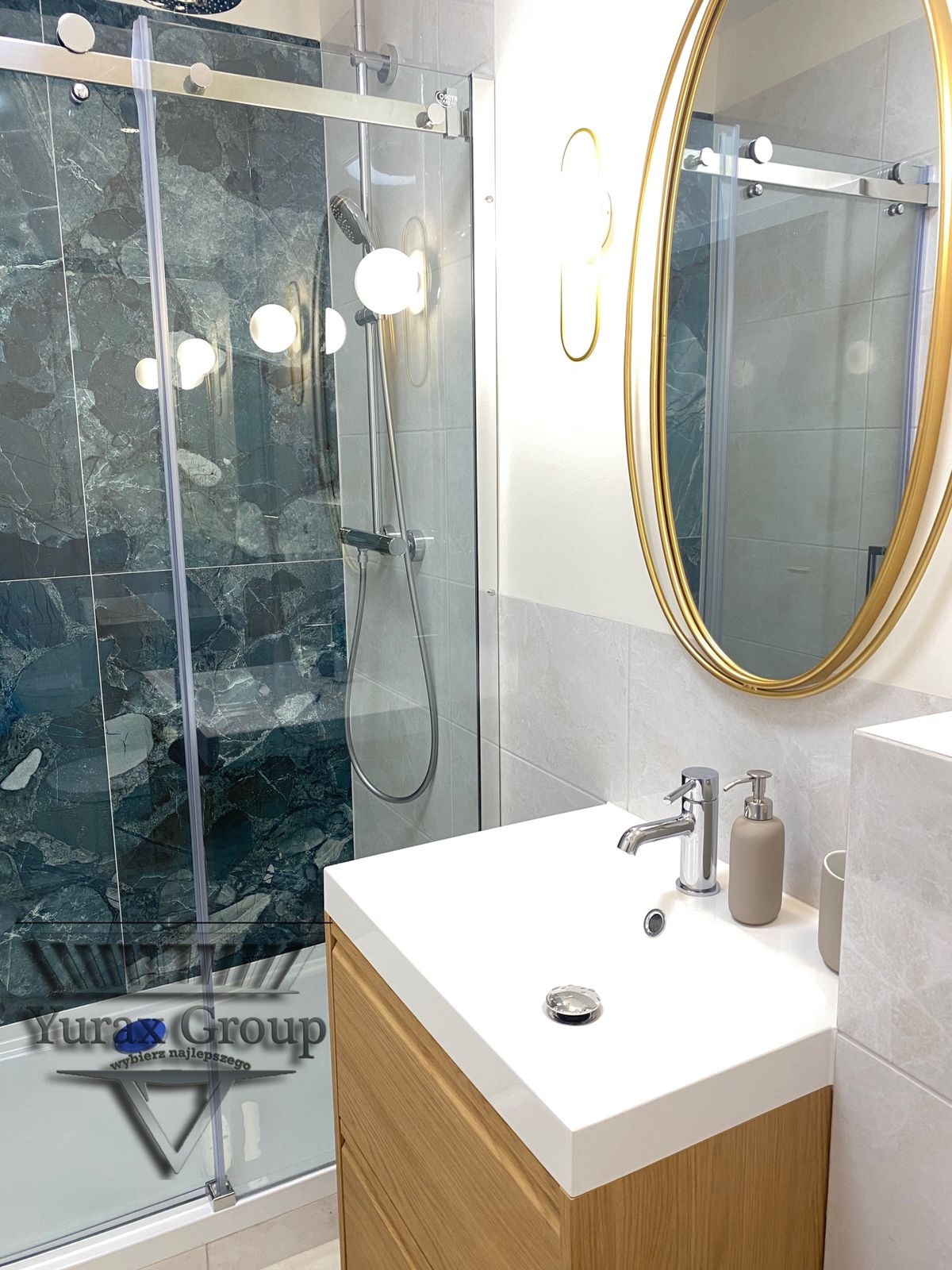 Wykończona łazienka w Sopocie z kabiną prysznicową z ciemnozielonymi płytkami imitującymi marmur, umywalką z szafką z jasnego drewna i owalnym lustrem w złotej ramie.