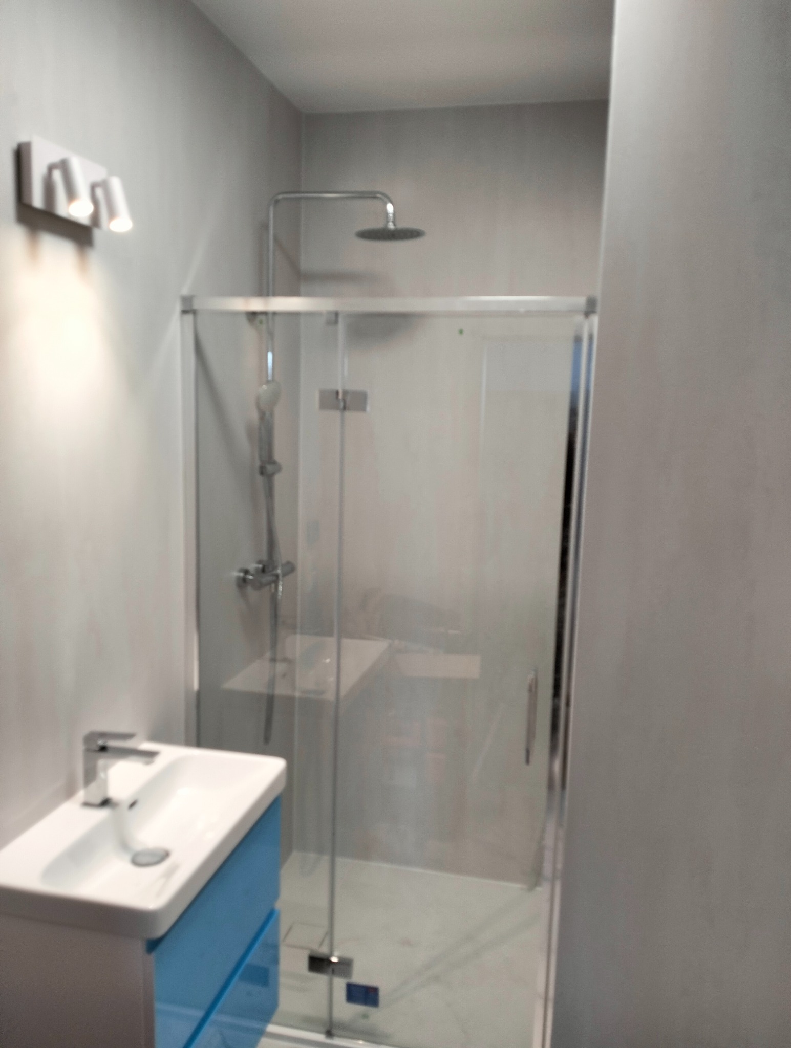 Nowoczesna łazienka z kabiną prysznicową typu walk-in, umywalką na szafce w kolorze błękitnym i oświetleniem punktowym.