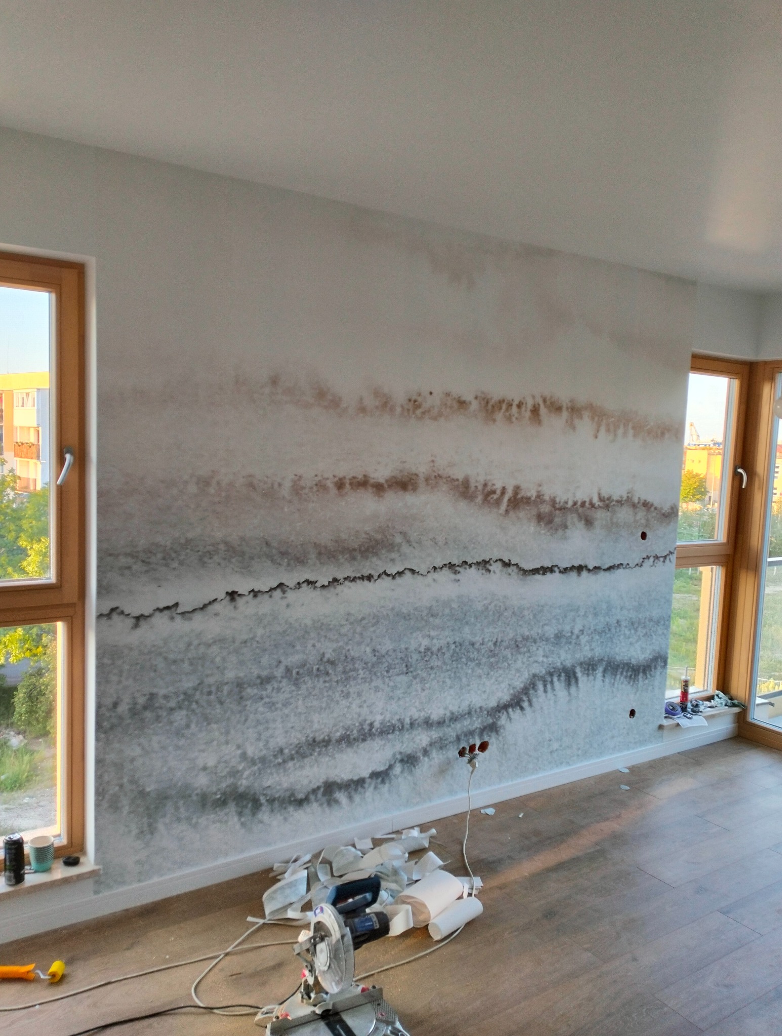 Ściana w pokoju po malowaniu dekoracyjnym imitującym warstwy geologiczne, widoczne wystające kable, narzędzia pracy i resztki materiałów na podłodze.