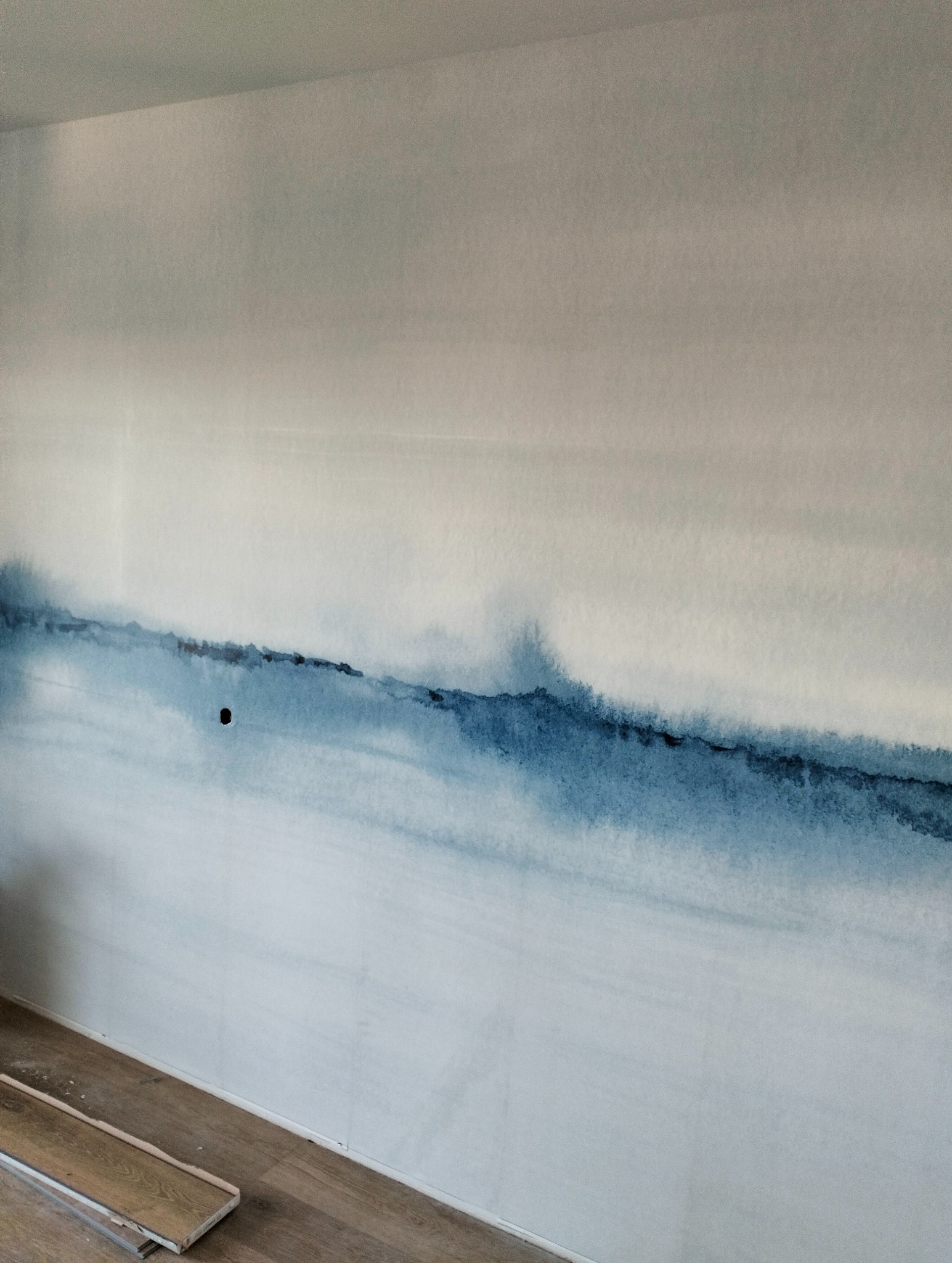 Ściana z efektem akwareli w odcieniach bieli i niebieskiego, widoczny otwór gniazdka elektrycznego i fragment podłogi z panelami.