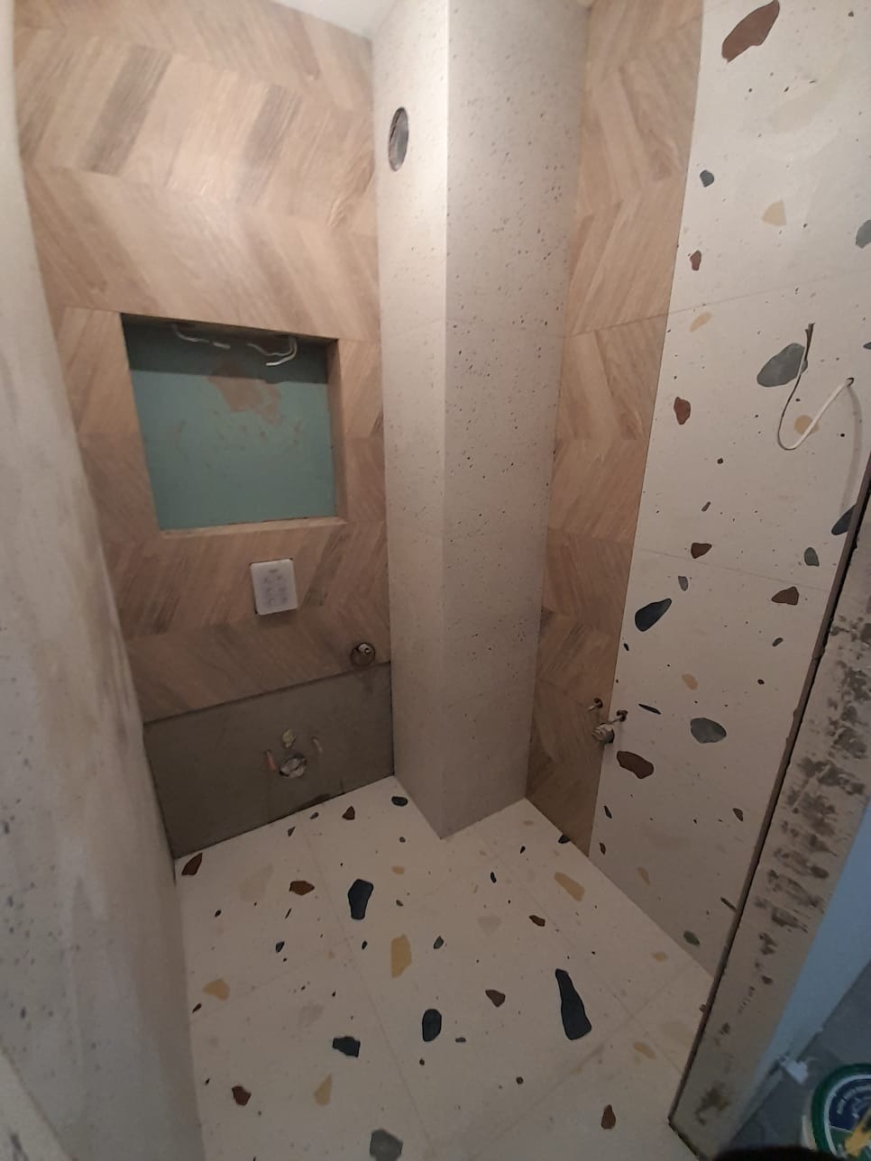 Wnętrze łazienki w trakcie prac wykończeniowych: ułożone płytki podłogowe w stylu lastryko, częściowo wykończone ściany z płytek imitujących drewno ułożonych w jodełkę oraz płytek w stylu lastryko,...