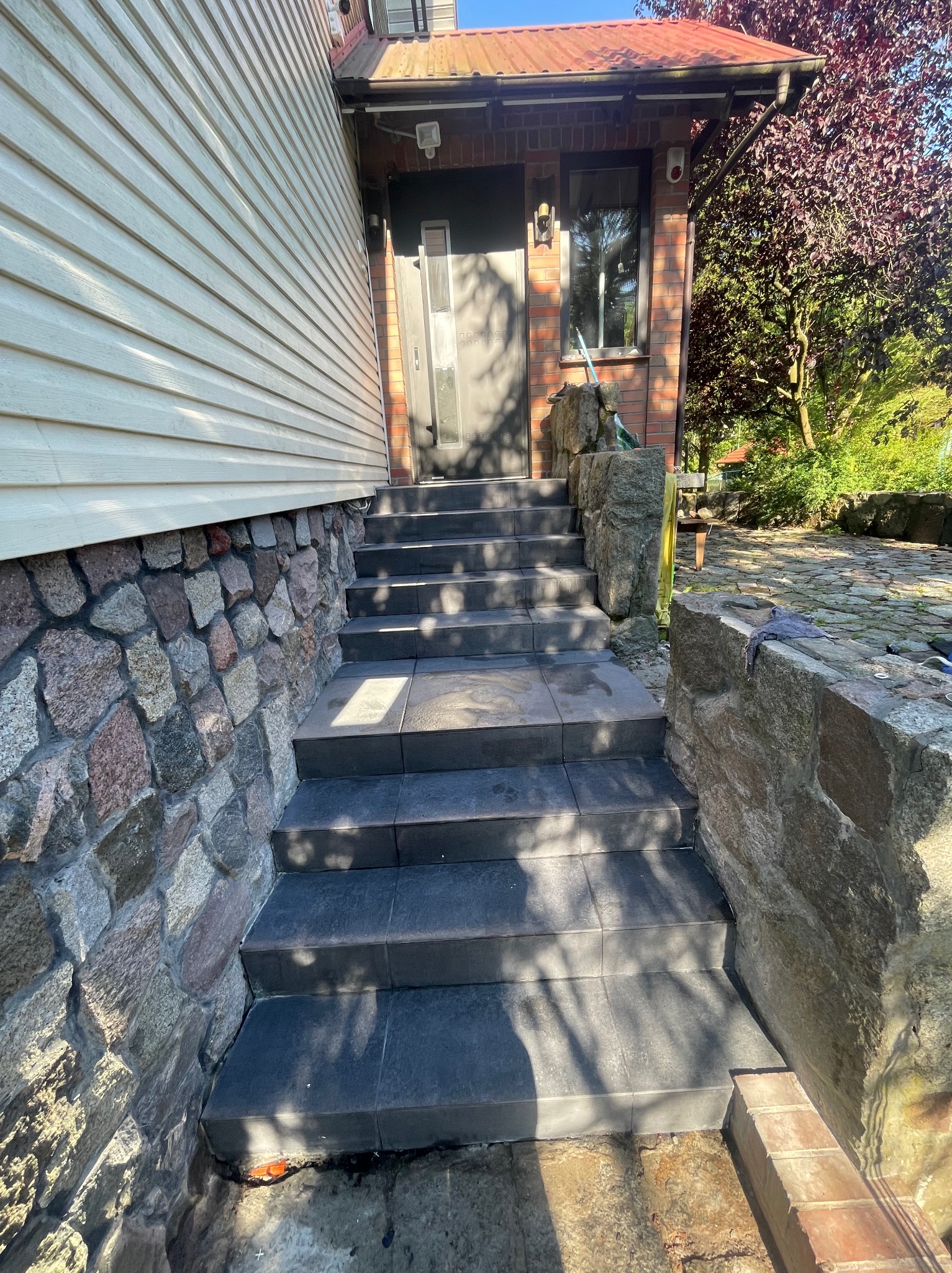 Granitowe schody wejściowe do domu z elementami kamiennymi, prowadzące do drzwi wejściowych. Widoczne detale wykończenia i otoczenie budynku.