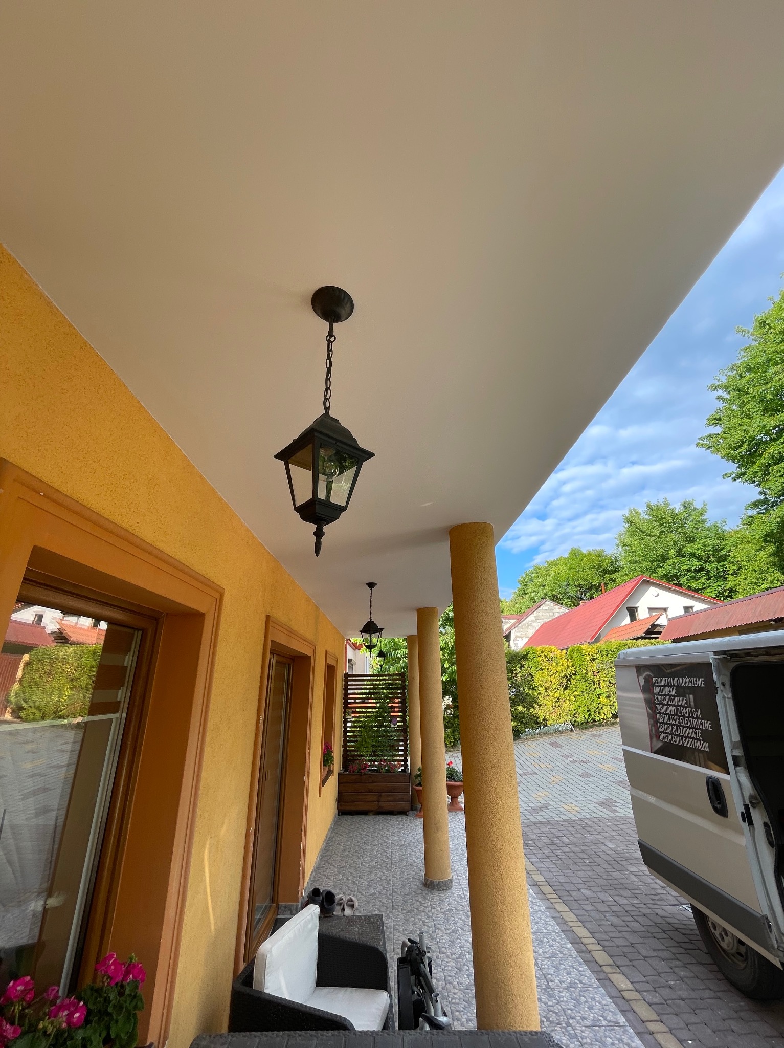 Odnowiony balkon z kolumnami i nowym oświetleniem zewnętrznym. Widoczny fragment samochodu z reklamą usług remontowo-wykończeniowych.