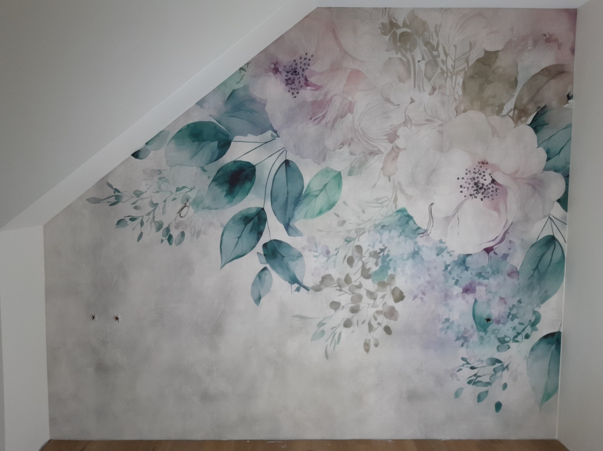 Ściana w pokoju na poddaszu pokryta tapetą z motywem akwarelowych kwiatów i liści w odcieniach bieli, zieleni i fioletu, z widocznymi niedoskonałościami na powierzchni tapety.