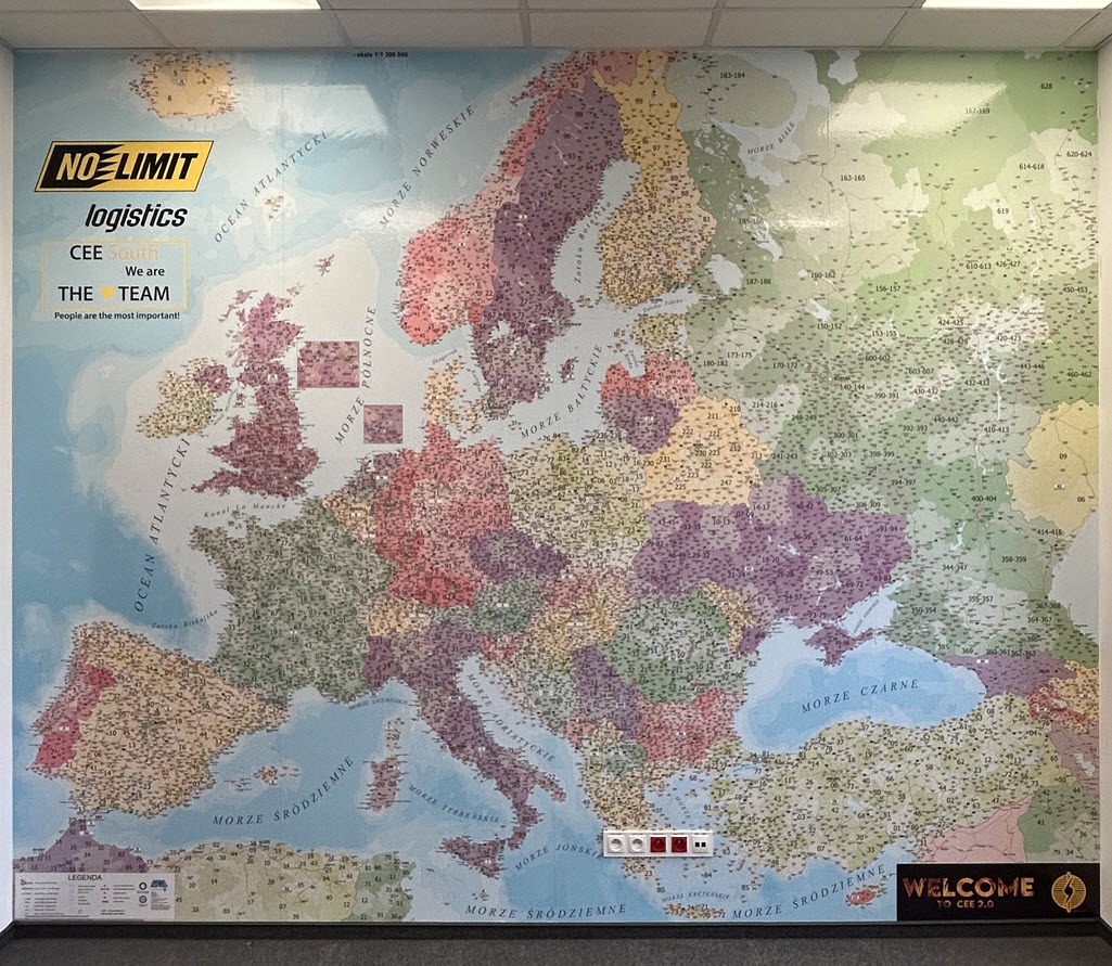 Biuro logistyczne: mapa Europy na ścianie, oznaczona numerami. Logo firmy No Limit Logistics. Element wystroju biura z hasłem 'We are the team'.