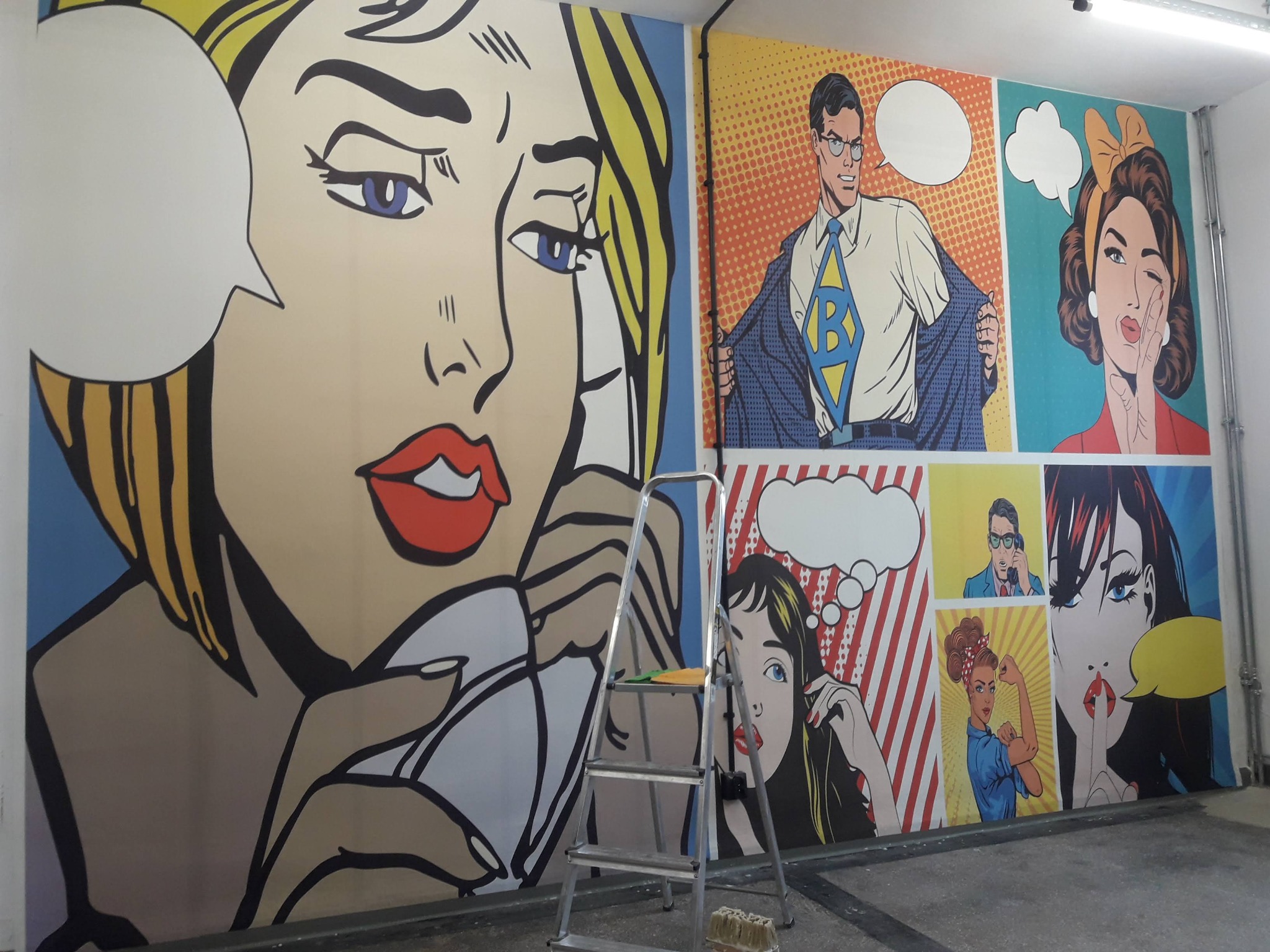 Ściana w stylu pop-art z komiksowymi postaciami, wykonana z użyciem tapet. Widoczna drabina malarska, co sugeruje świeżo zakończone prace dekoracyjne.