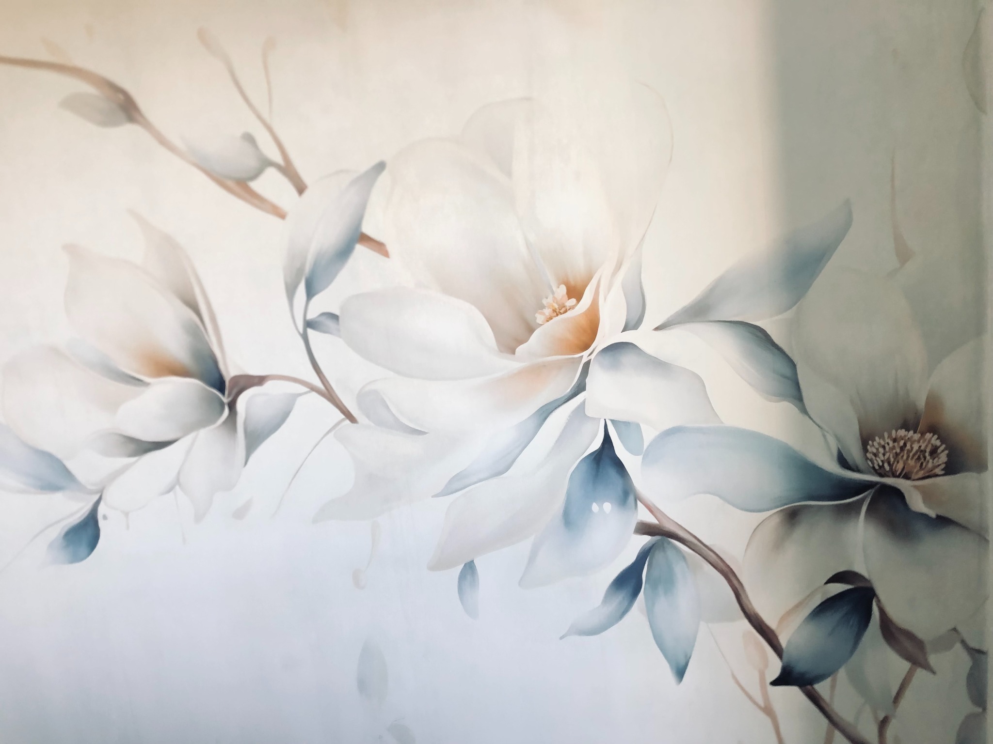 Delikatne, ręcznie malowane magnolie na ścianie, subtelne przejścia kolorystyczne, miękkie światło, artystyczny akcent w jasnym wnętrzu.