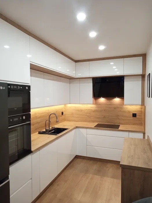 Nowoczesna kuchnia z białymi, lakierowanymi szafkami i drewnianym blatem oraz podświetleniem LED pod szafkami wiszącymi.