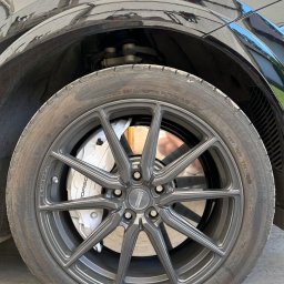 Brand New Car - Czarny samochód z szarą felgą Vossen i białymi zaciskami hamulcowymi Porsche, widoczne opony Bridgestone.