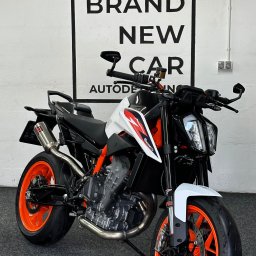 Brand New Car - Nowoczesny motocykl KTM z pomarańczowymi felgami na tle białej ściany z czarnym napisem 'BRAND NEW CAR AUTODET'