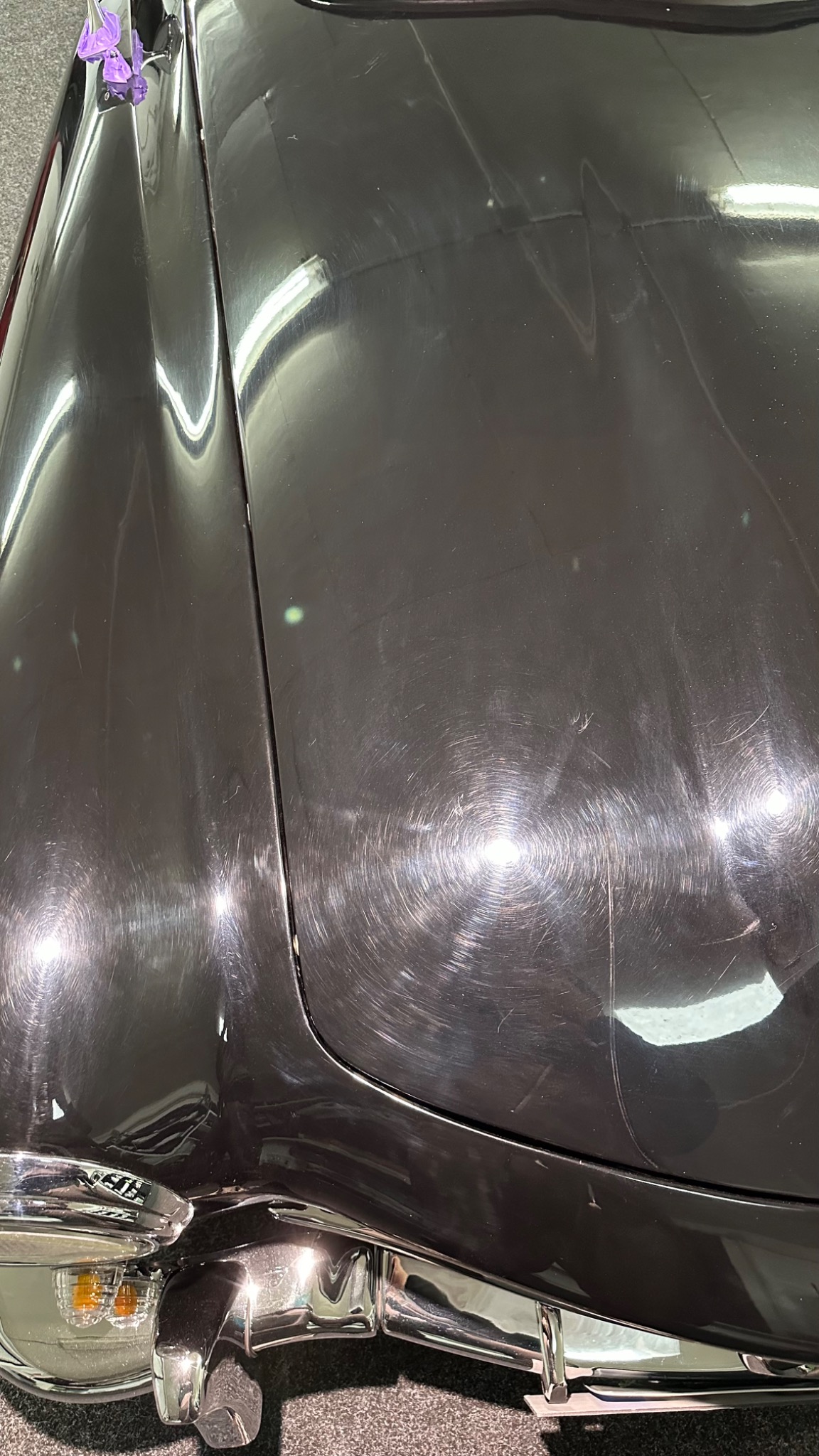 Czarny lakier samochodu z widocznymi śladami polerowania w okrągłe wzory, przednia część pojazdu z chromowanymi elementami i reflektorem.