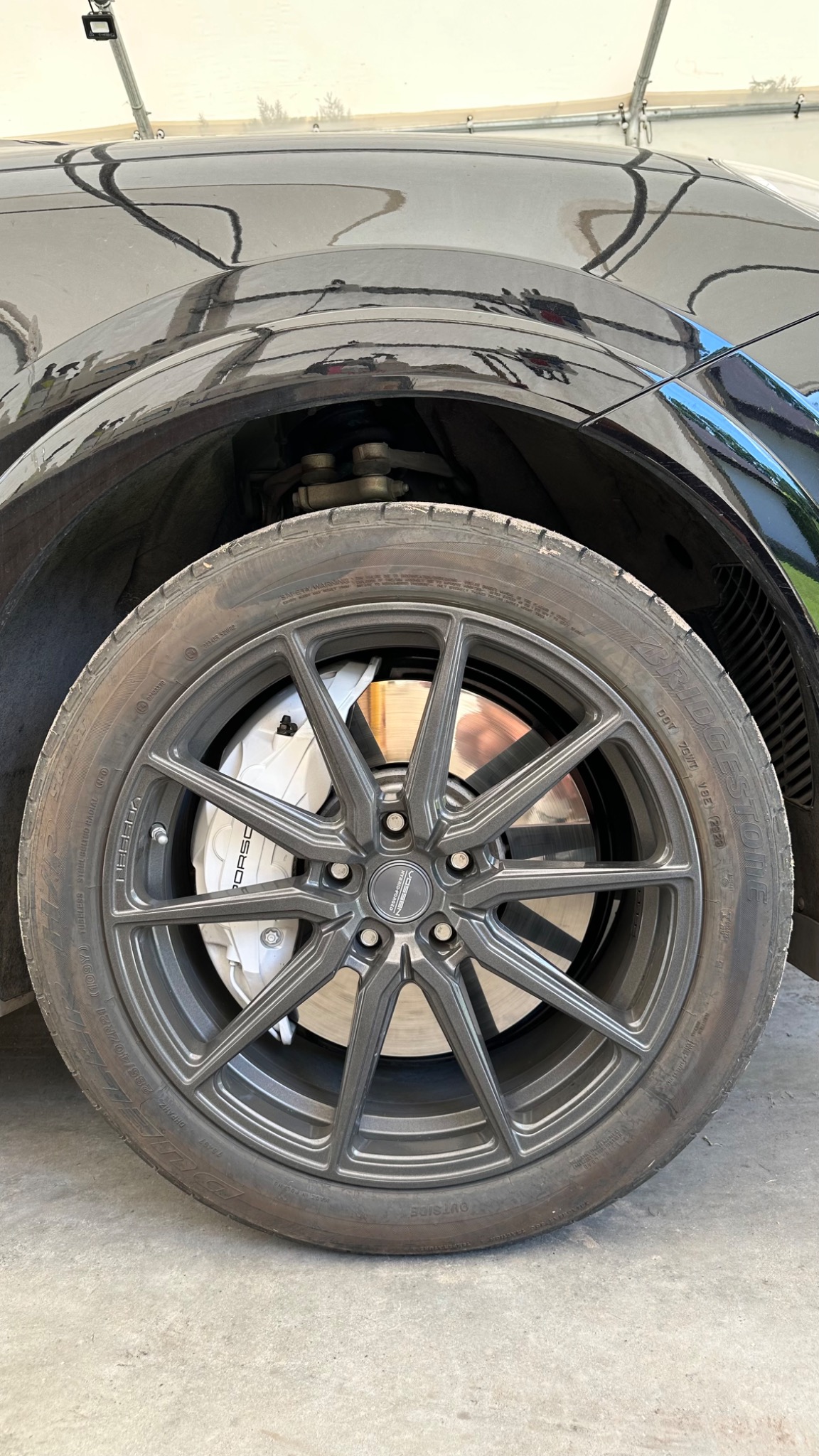 Czarny samochód z szarą felgą Vossen i białymi zaciskami hamulcowymi Porsche, widoczne opony Bridgestone.