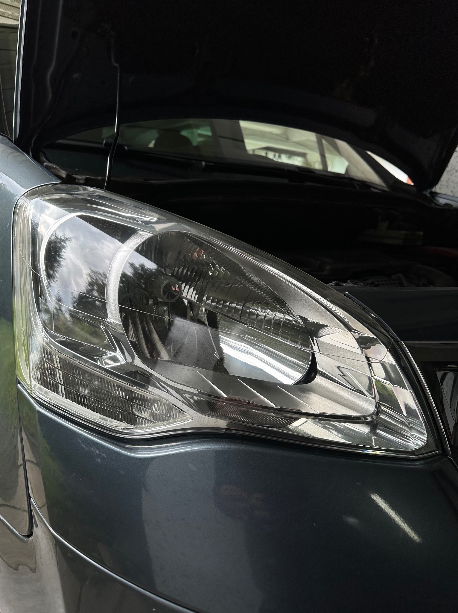 Szczegółowe ujęcie reflektora i fragmentu karoserii szarego samochodu z otwartą maską w Wolborzu, widoczne drobne zabrudzenia na lakierze.