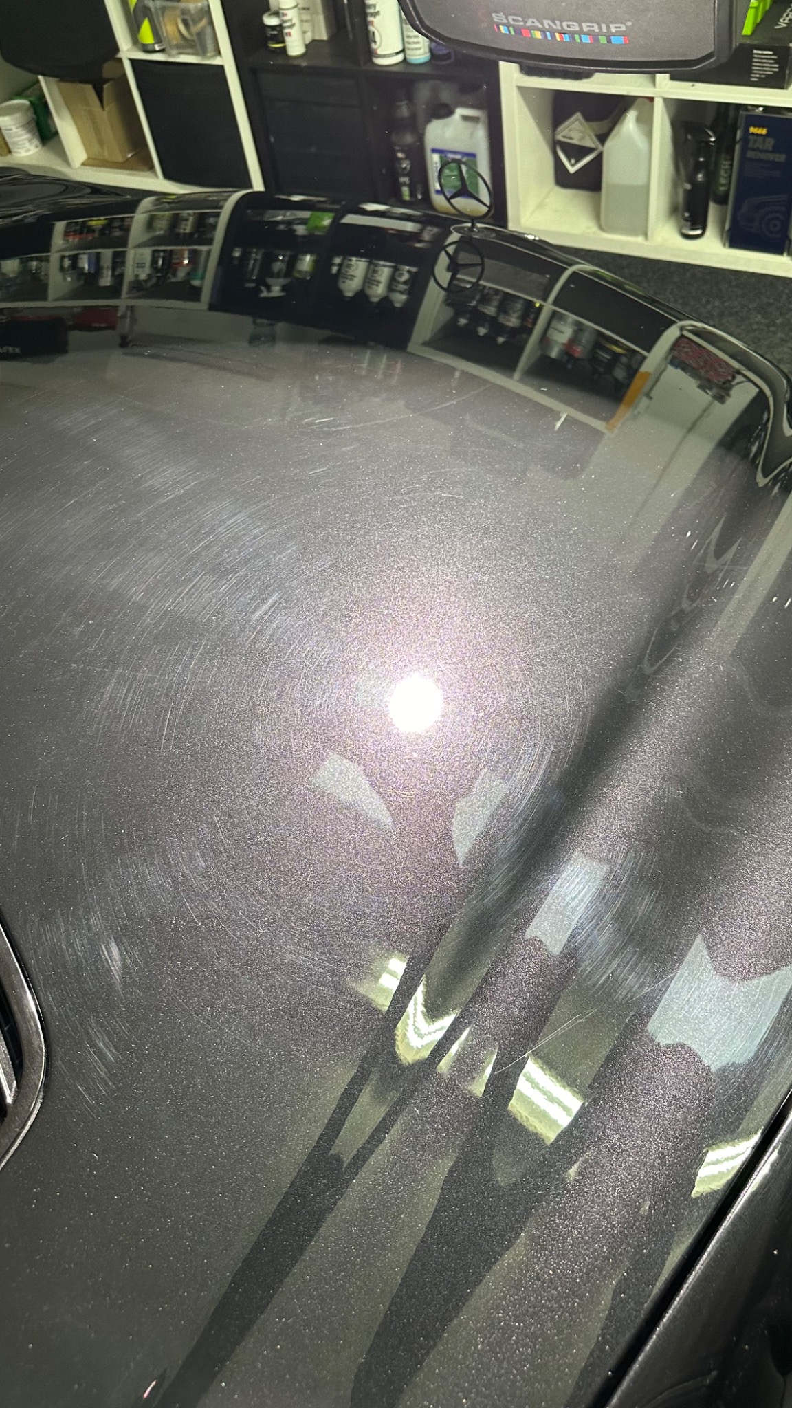 Powierzchnia lakieru samochodu z widocznymi kolistymi zarysowaniami, odbijająca oświetlenie warsztatowe przed procesem polerowania.