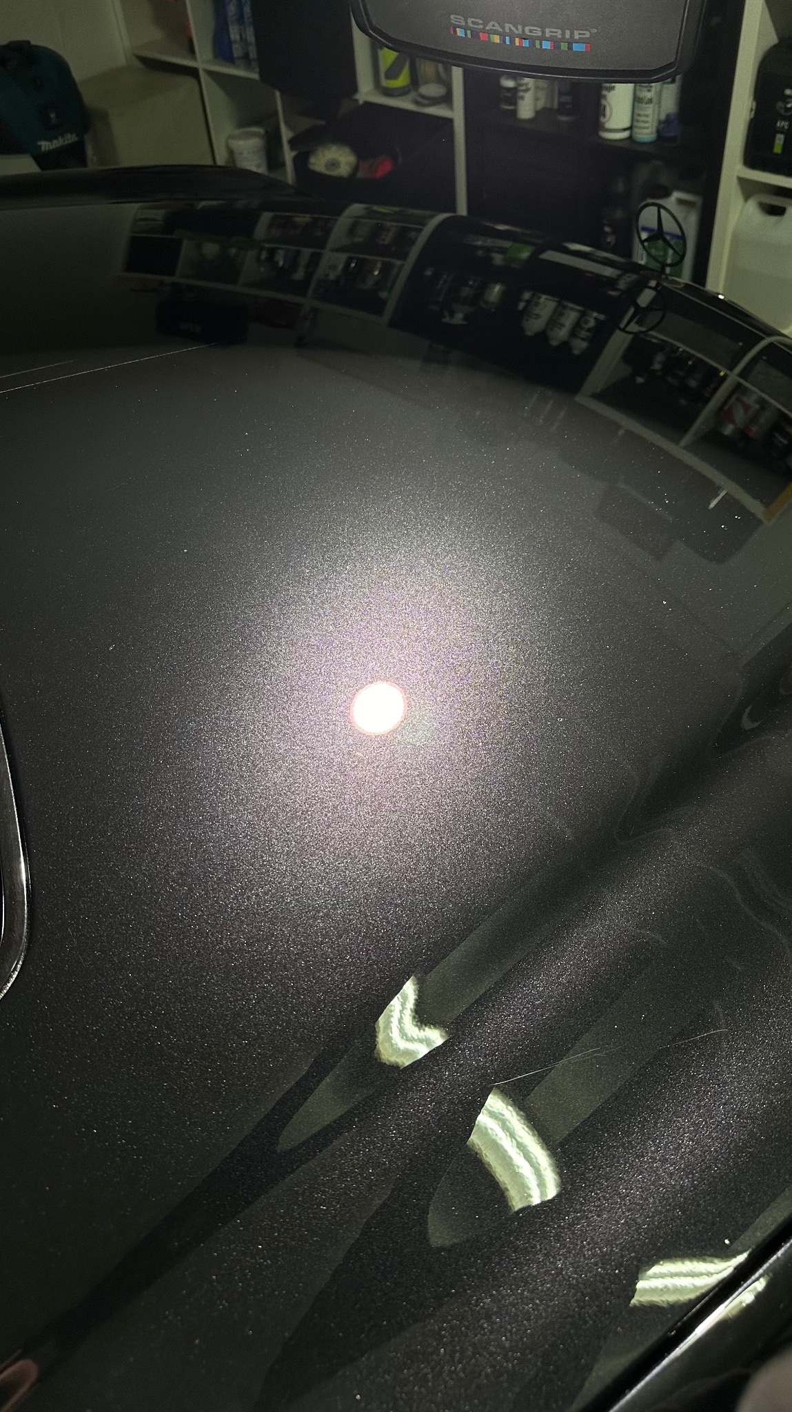 Błyszcząca, ciemnoszara powierzchnia karoserii samochodu po polerowaniu, odbijająca światło lampy warsztatowej, z widocznymi refleksami i minimalnymi niedoskonałościami lakieru.