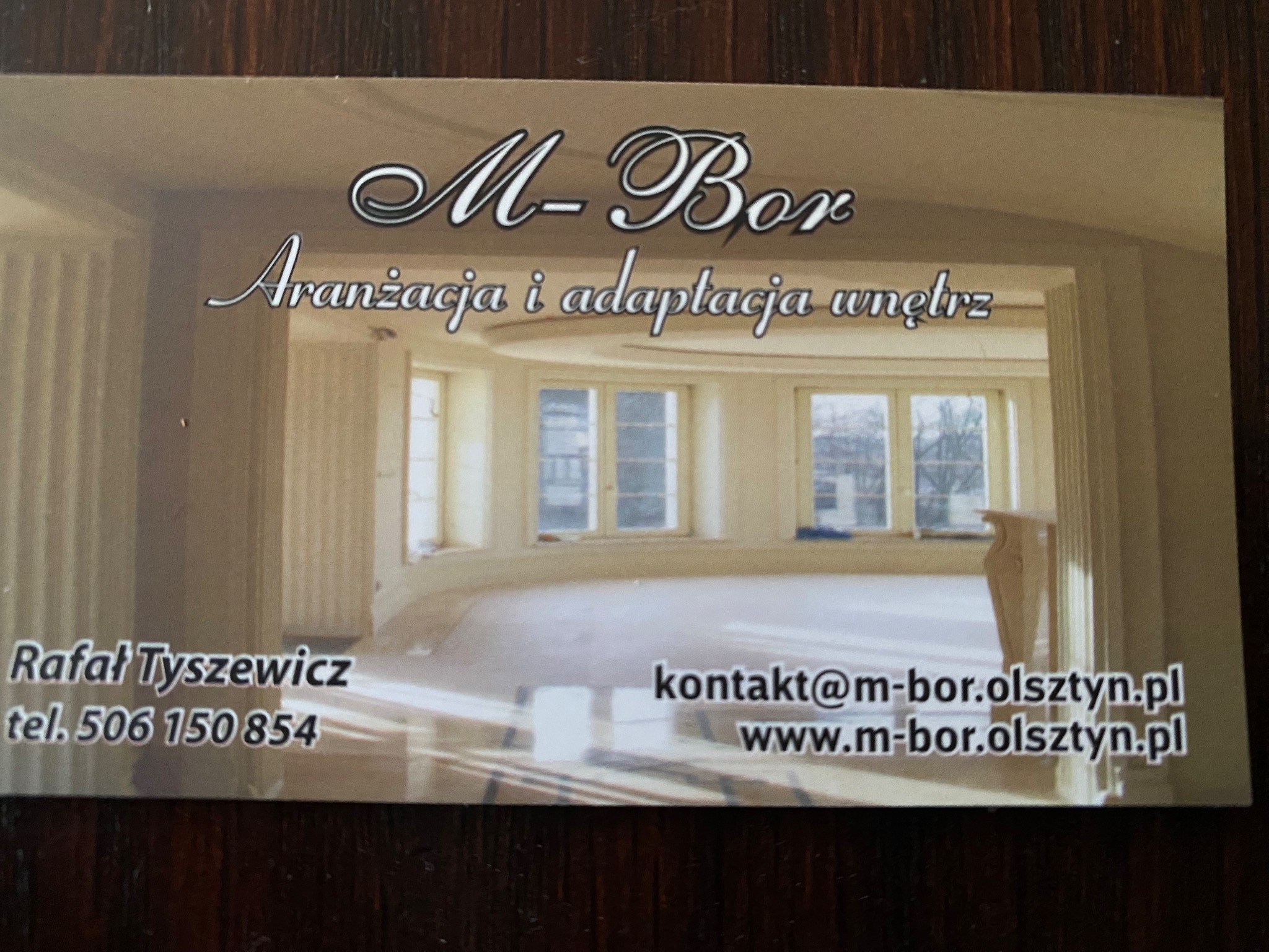 Wizytówka firmy M-Bor z Olsztyna, specjalizującej się w aranżacji i adaptacji wnętrz. Na zdjęciu widoczny fragment wnętrza z kolumnami i dużymi oknami.