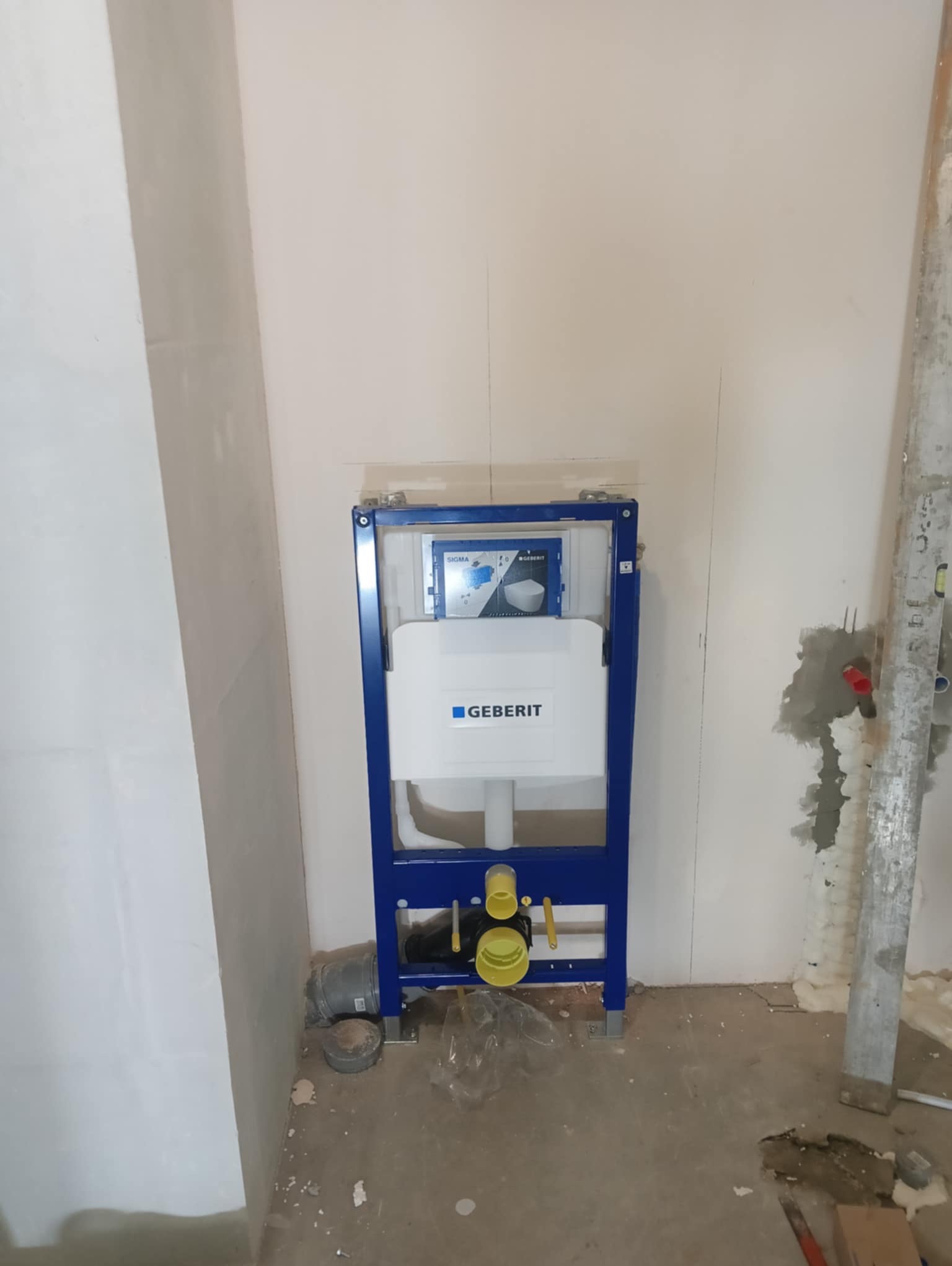 Stelaż podtynkowy Geberit zamontowany w surowej łazience, widoczne rury kanalizacyjne i ściany przygotowane pod wykończenie.