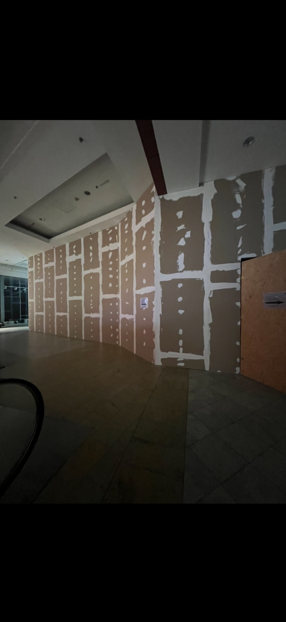 Montaż płyt karton-gips na zakrzywionej ścianie w dużym pomieszczeniu. Widoczne łączenia płyt wypełnione masą szpachlową. Na ścianie naklejki informacyjne.