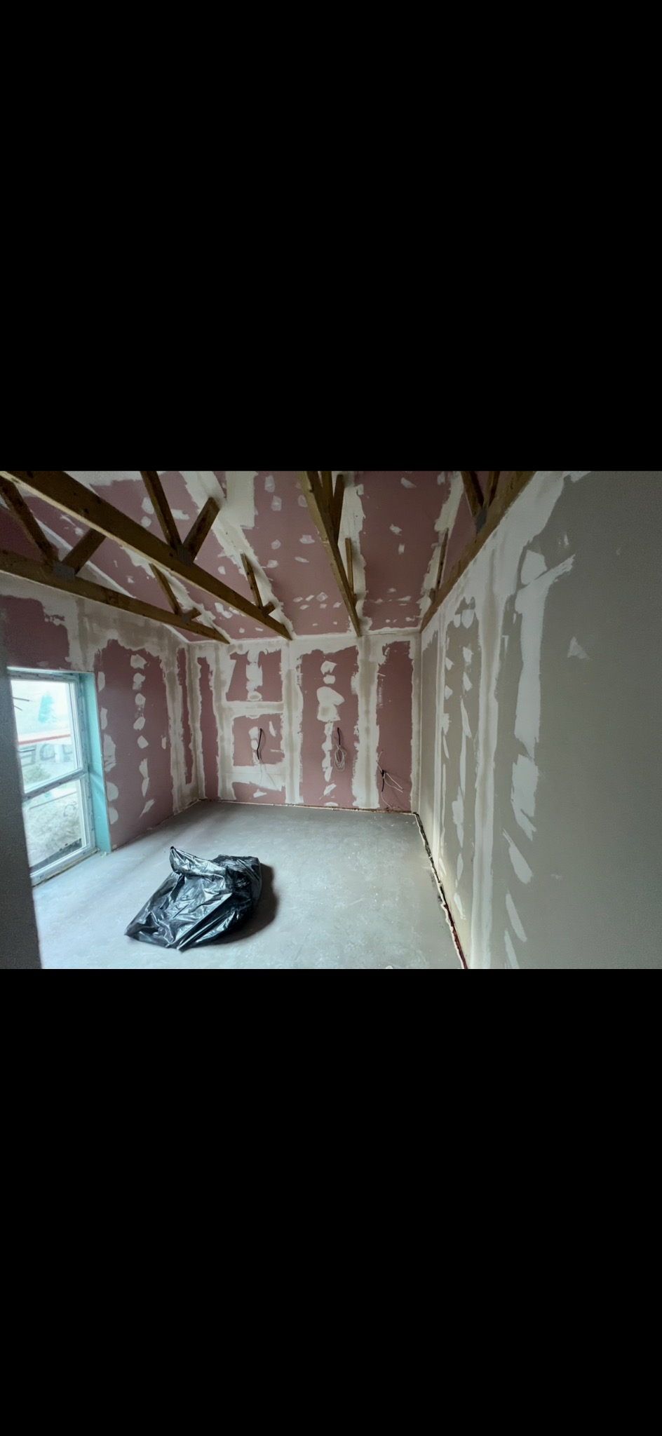 Pokój w trakcie prac wykończeniowych: ściany z płyt kartonowo-gipsowych, częściowo pokryte gładzią, widoczne drewniane elementy konstrukcyjne dachu i czarny worek na podłodze.