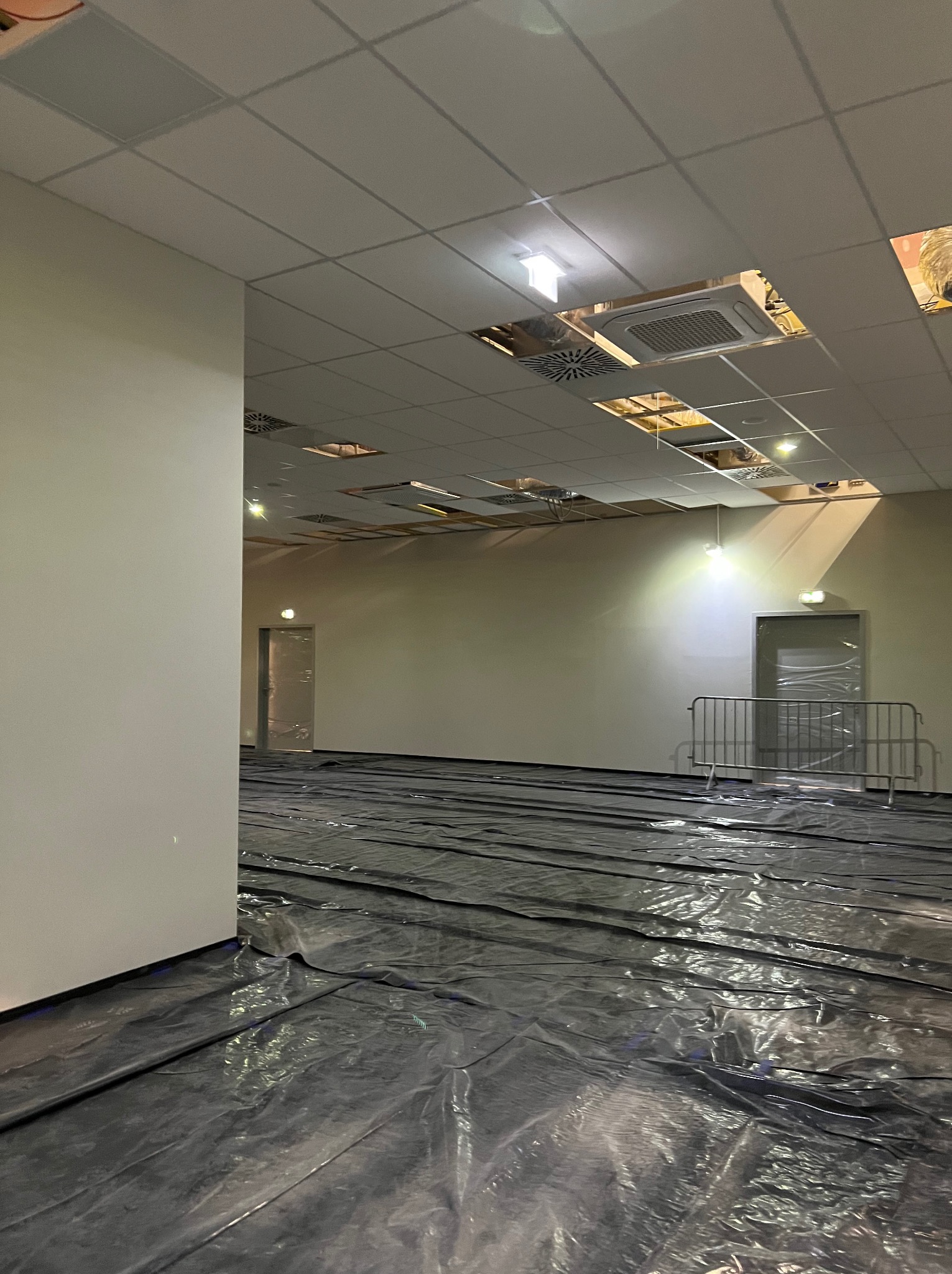 Przygotowanie do prac w dużym pomieszczeniu biurowym: podłoga zabezpieczona folią, widoczne elementy instalacji pod sufitem. Oświetlenie sufitowe.