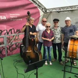 Zespół muzyczny 'Słowianin' na scenie z kontrabasem i perkusją, na tle różowego baneru Szczecińskiej Agencji Artystycznej.