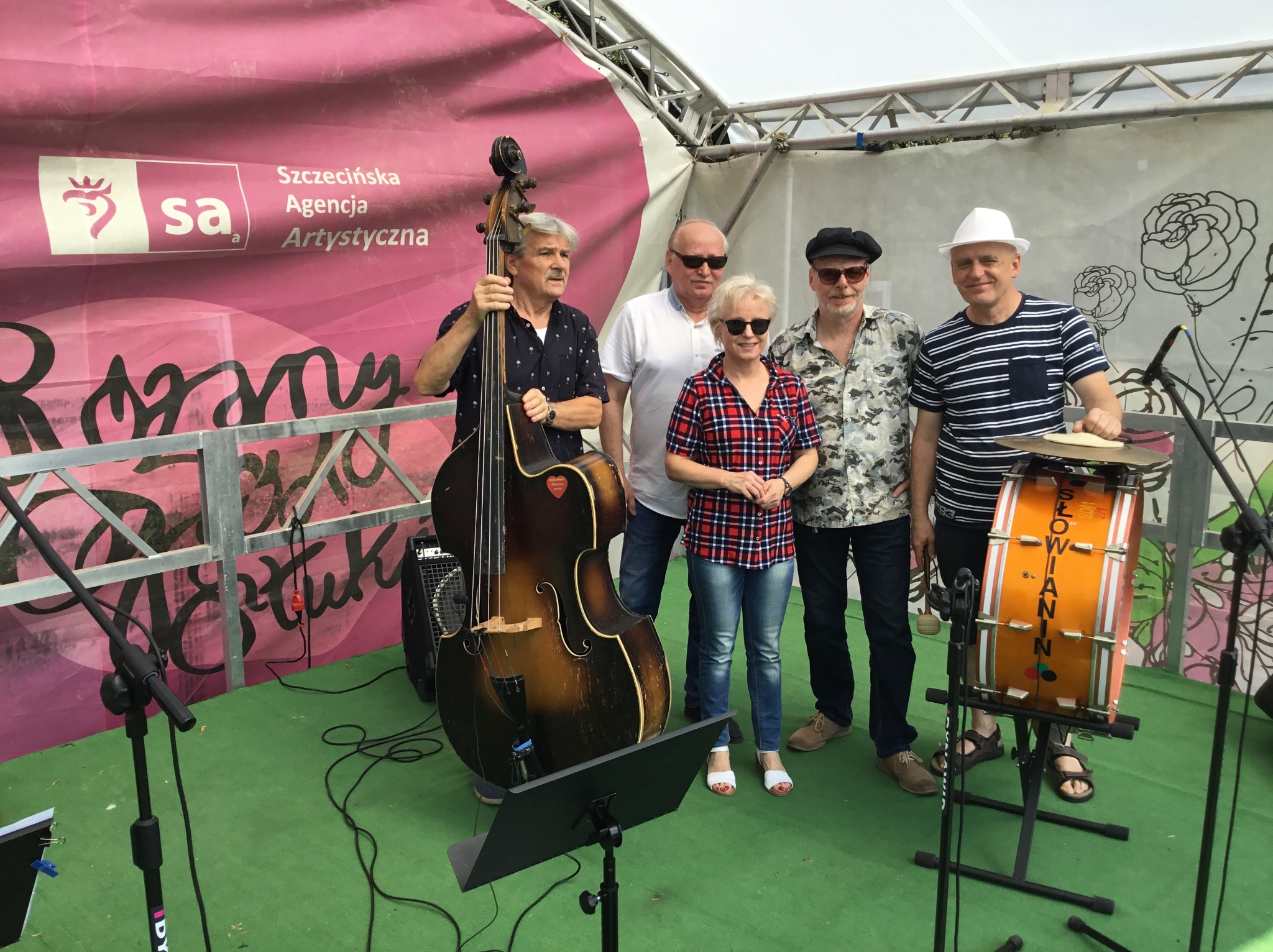 Zespół muzyczny 'Słowianin' na scenie z kontrabasem i perkusją, na tle różowego baneru Szczecińskiej Agencji Artystycznej.